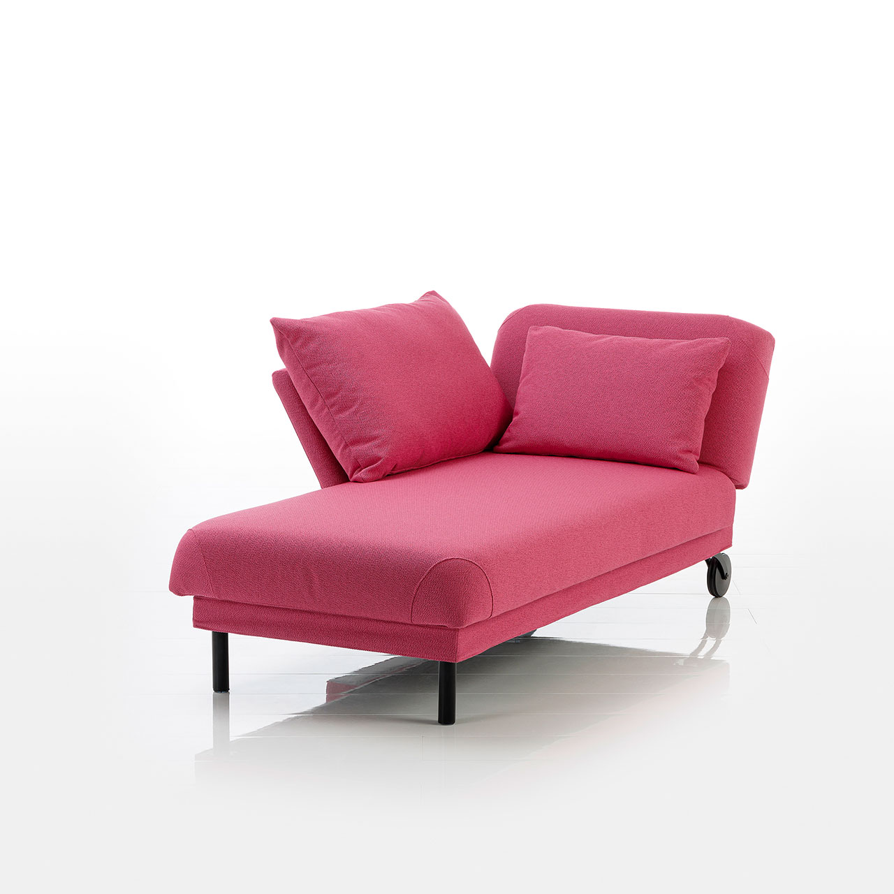 Recamiere in pinkem Stoff mit Rollen an der Kopfseite und zylindrischen Füßen an der Fußseite. Das Kopfteil ist höhenverstellbar. Links vom Kopfteil ist eine abklappbare Armlehne angebracht.