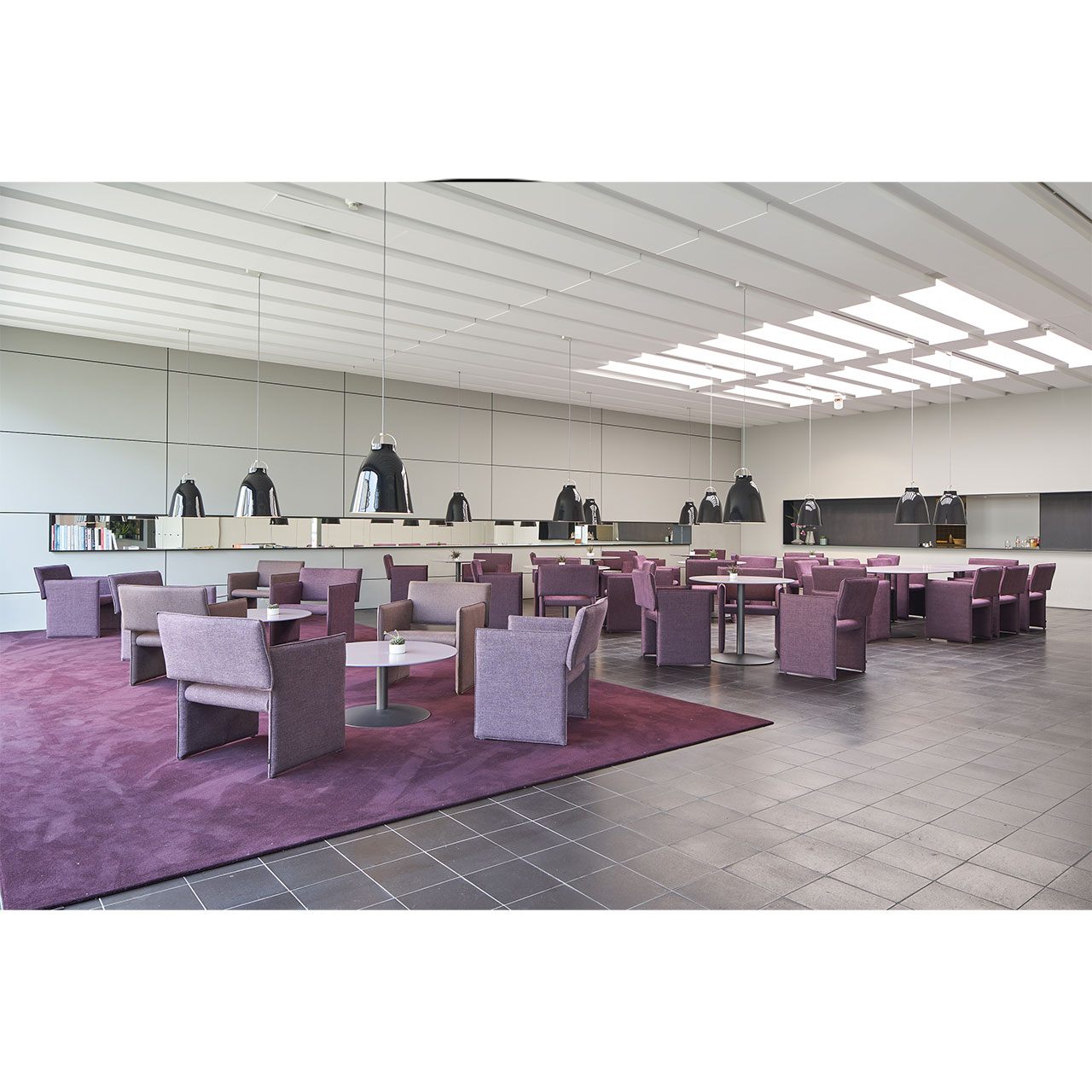 Eine große Anzahl von Noto Stühlen in gleichem Rot-Ton, die um runde Tische stehen, in Bistro-Atmosphäre.