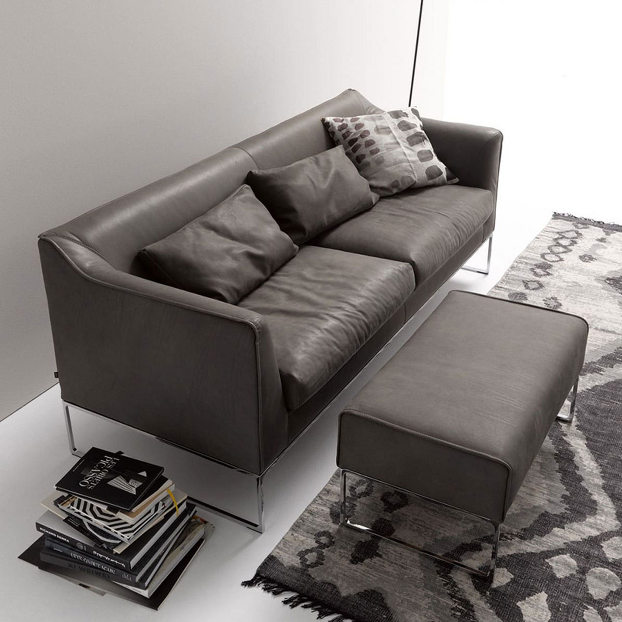 Sofa mit passendem Hocker mit Dekoration in einem Wohnzimmer. Alles mit dunklem Lederbezug. Hocker Rechteckig auf Chromkufen wie das Sofa.