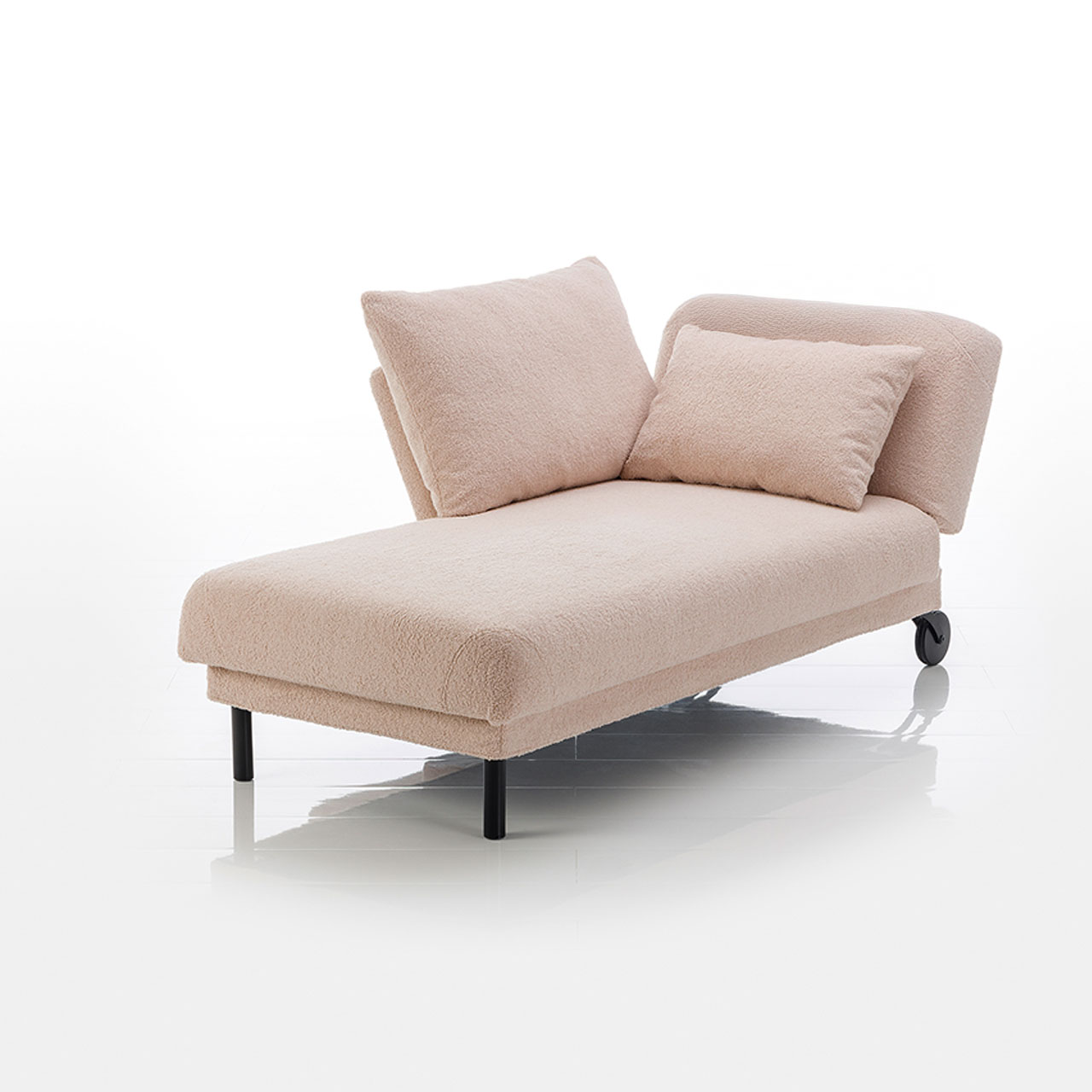 Recamiere in hellbraunem Stoff mit Rollen an der Kopfseite und zylindrischen Füßen an der Fußseite. Das Kopfteil ist höhenverstellbar. Links vom Kopfteil ist eine verschiebbare Armlehne angebracht.