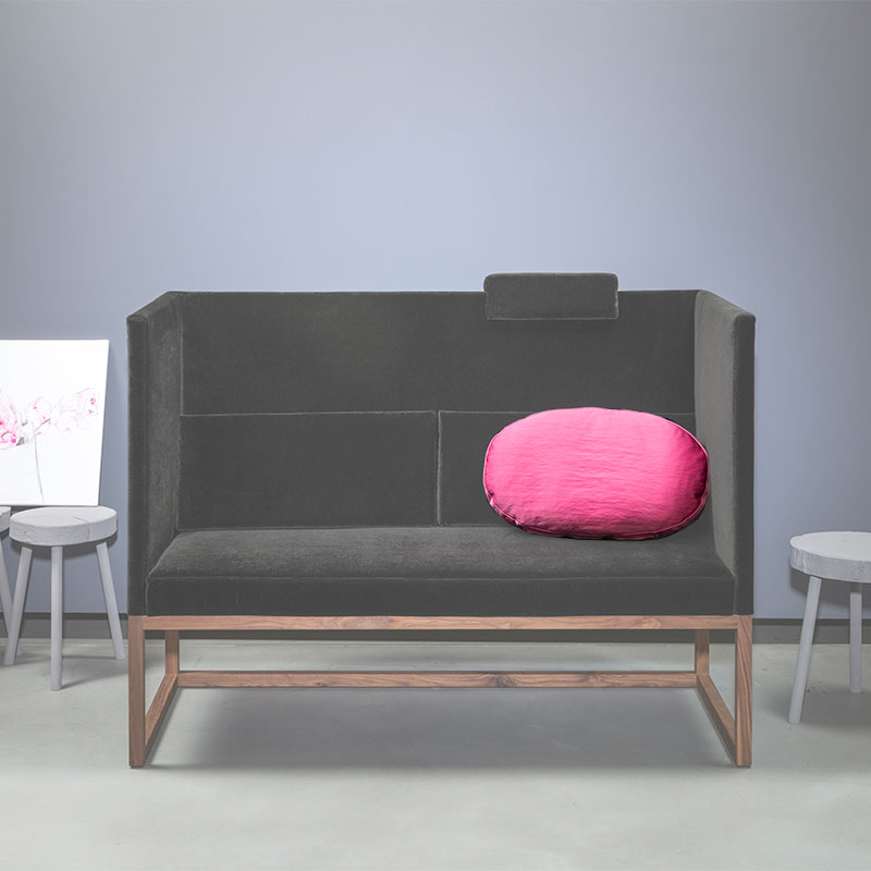 Eine Bank mit hoher Rücken- und Seitenlehnen mit einem Kissen. Die Bank ist leicht ausgegraut um das pinke Kissen hervorzuheben.