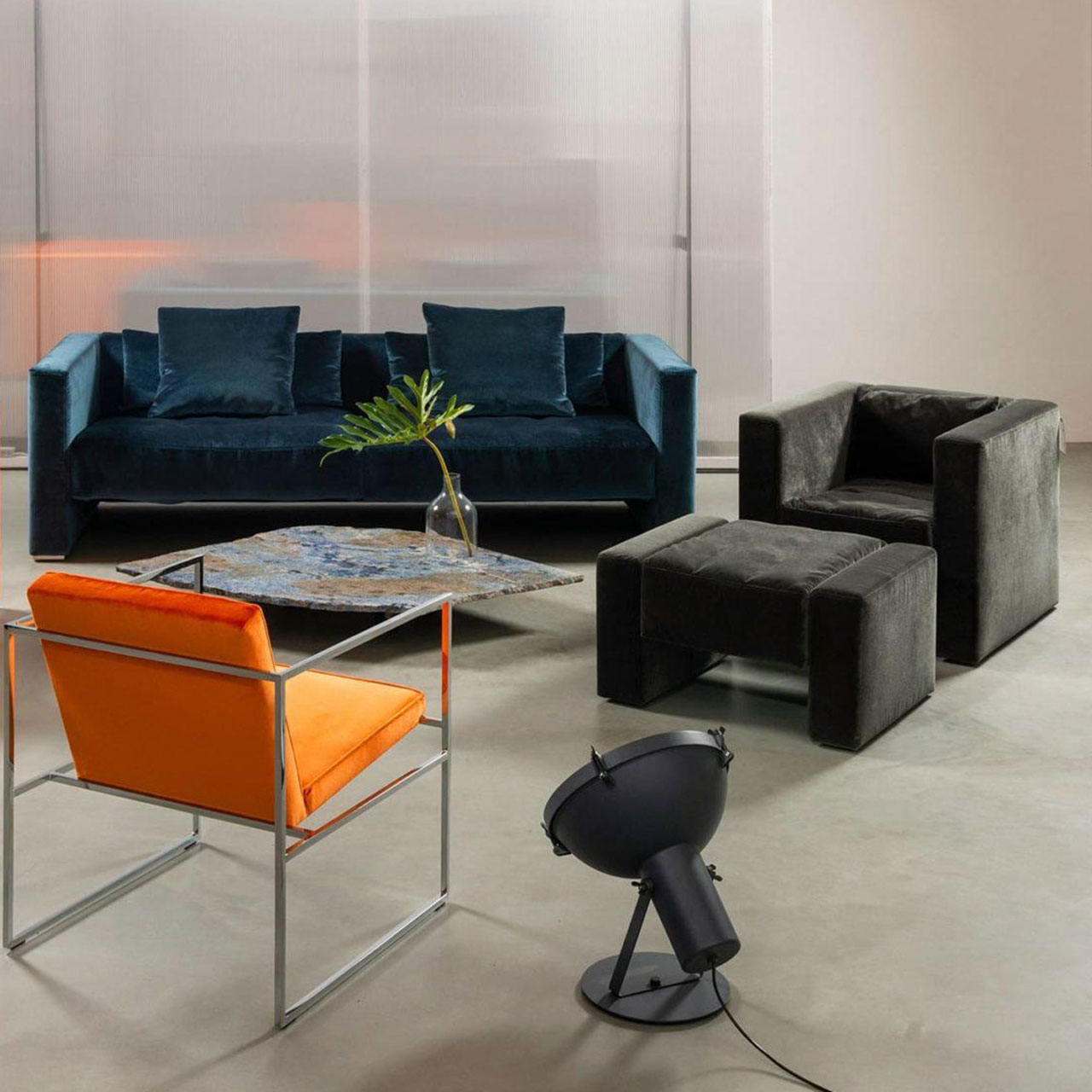 Ambientebild. Im Hintergrund stehen ein Sofa und ein Wohnzimmertisch. Der Fokus liegt auf einem schwarzen Sessel mit dazu passendem Hocker.