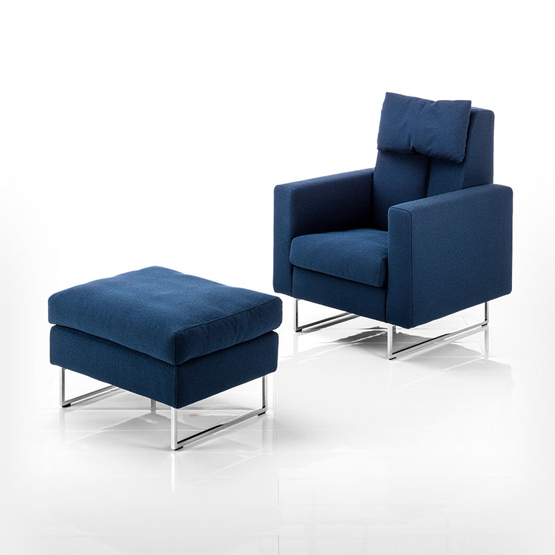 Hochlehnsessel mit zwei Kufen in Edelstahl mit dazu passendem Hocker. Beide Sitzmöbel sind mit dunkelblauem Stoff bezogen.