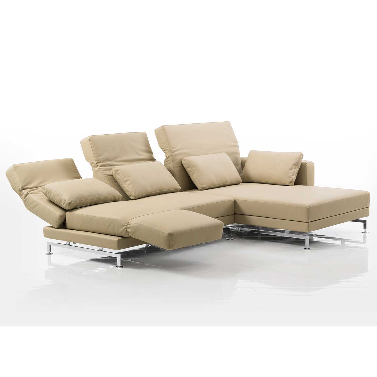 Eckgarnitur mit breitem Longchair rechts und in beigem Leder. Die mittlere und linke Rückenlehne sind teilweise abgesenkt. Die linke Armlehne ist zur Fußstütze vorgeschwenkt.