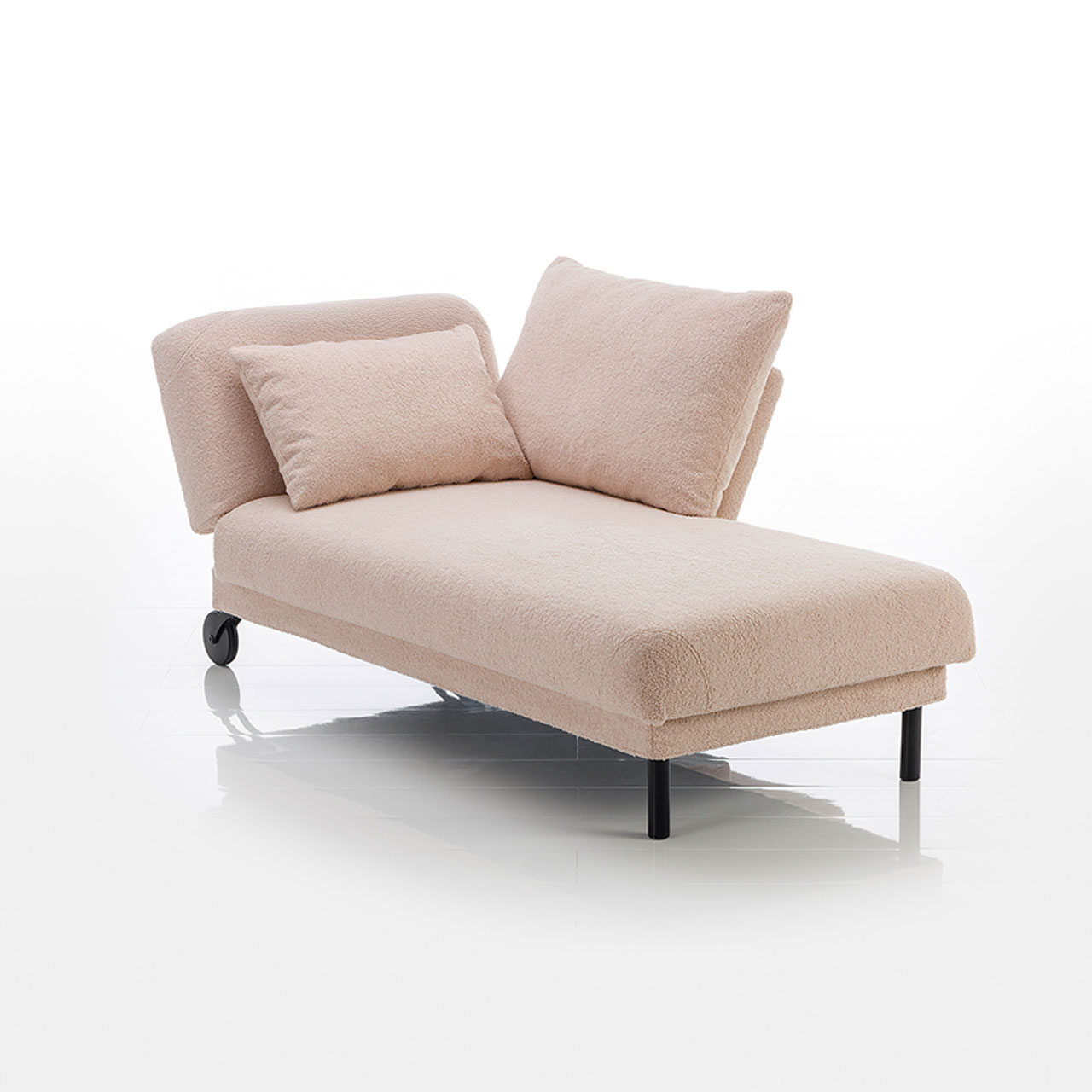 Recamiere in hellbraunem Stoff mit Rollen an der Kopfseite und zylindrischen Füßen an der Fußseite. Das Kopfteil ist höhenverstellbar. Rechts vom Kopfteil ist eine verschiebbare Armlehne angebracht.