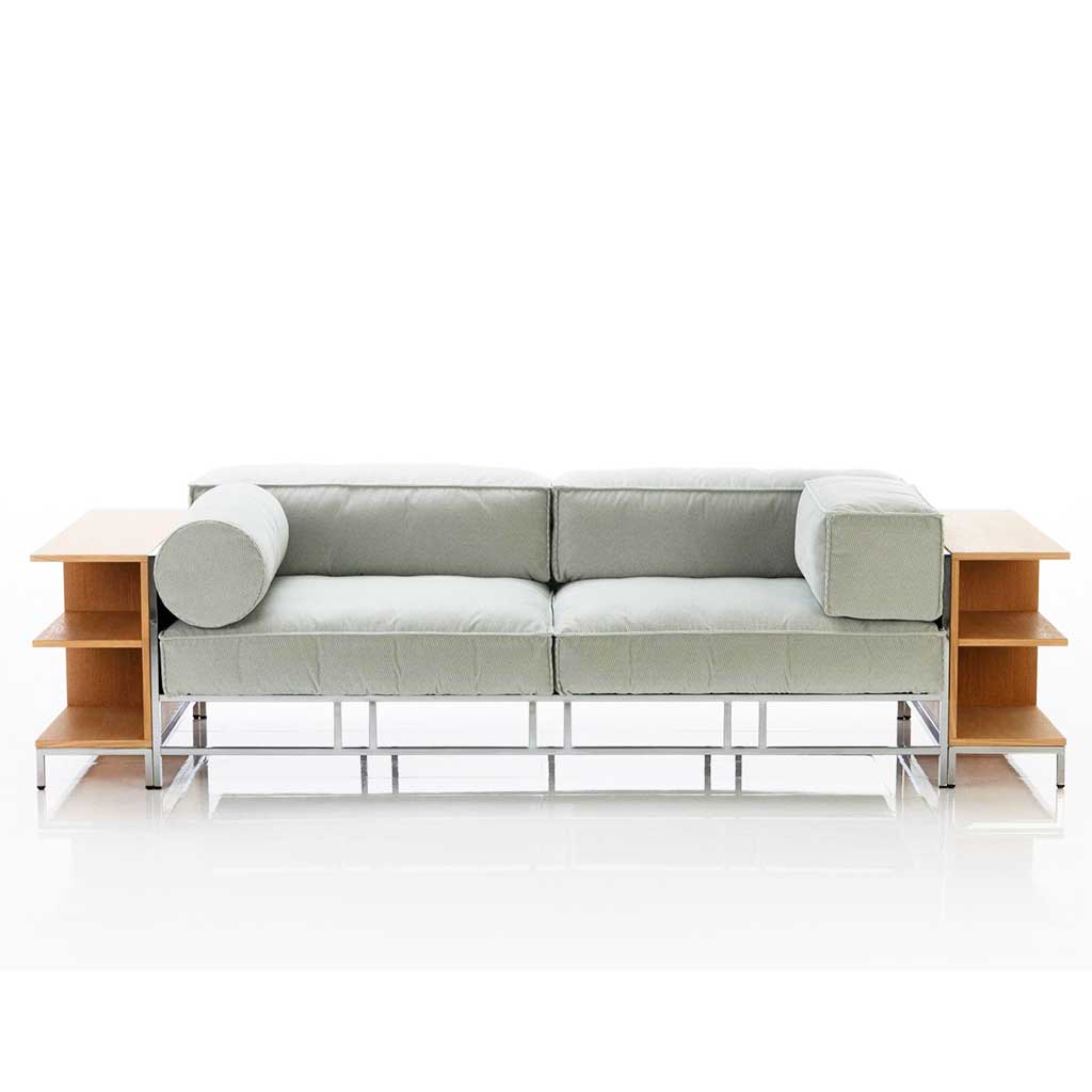 Sofa mit Polstern in hellem mint und chrom glänzendem Untergestell. Rechts und links neben dem Sofa ist je ein niedriges, offenes Regal an das Sofa angestellt. 