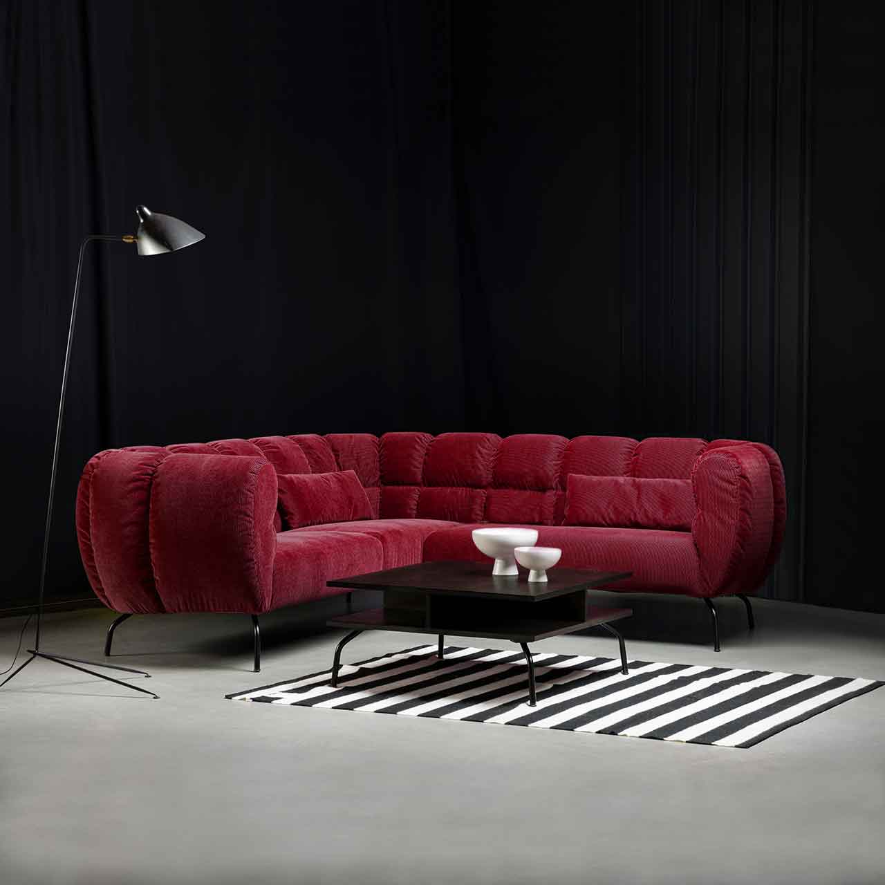 Ambientebild: Eckgarnitur von brühl magnolia in dunkelrotem Stoff mit schwarzen Metallfüßen. Davor steht ein quadratischer Tisch mit dunkler Tischplatte und schwarzen Metallfüßen.