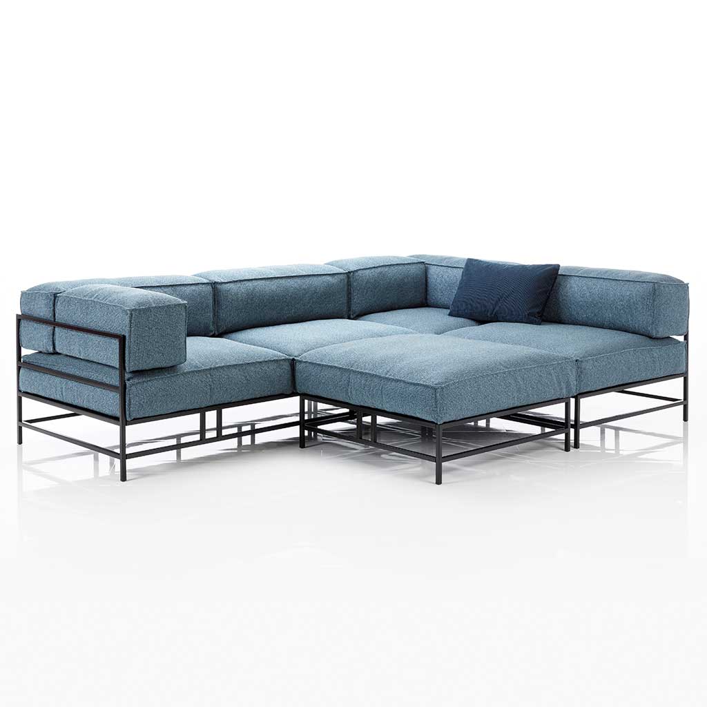 L-förmige Garnitur mit blauen Polstern und schwarzem Metallgestell. Vor den mittleren Sitzplatz ist ein passender Hocker angestellt.