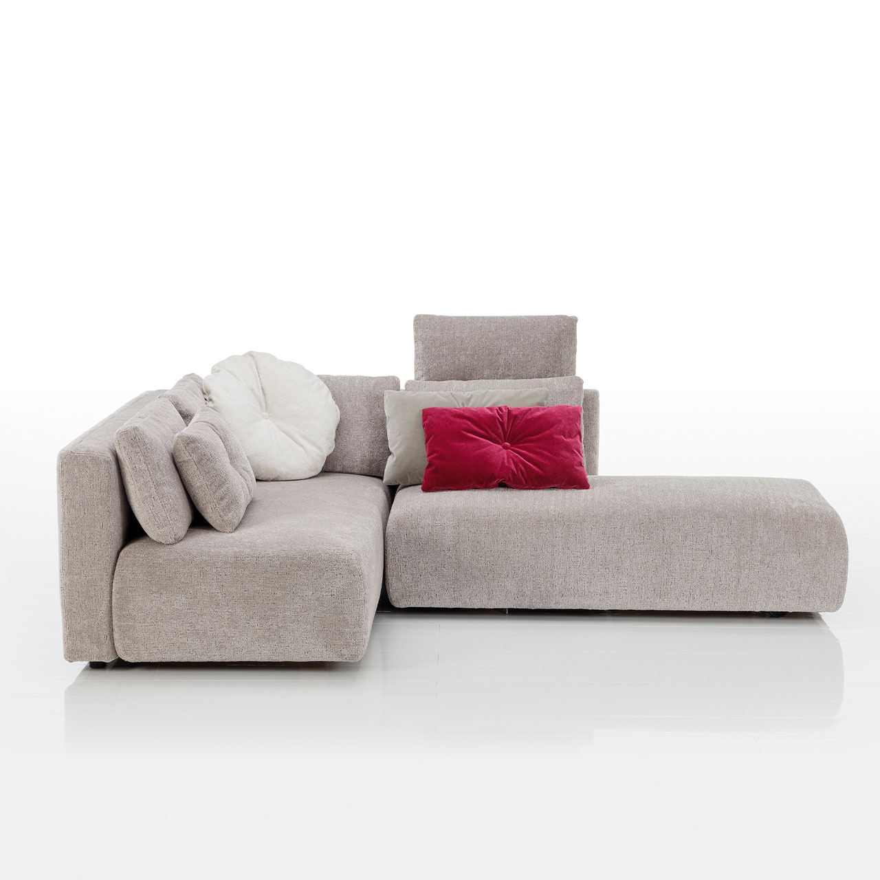 Bodennahes beiges Eckofa mit Longchair links und Drehsofa rechts. Auf dem Sofa liegen drei eckige und eine rundes Kissen.