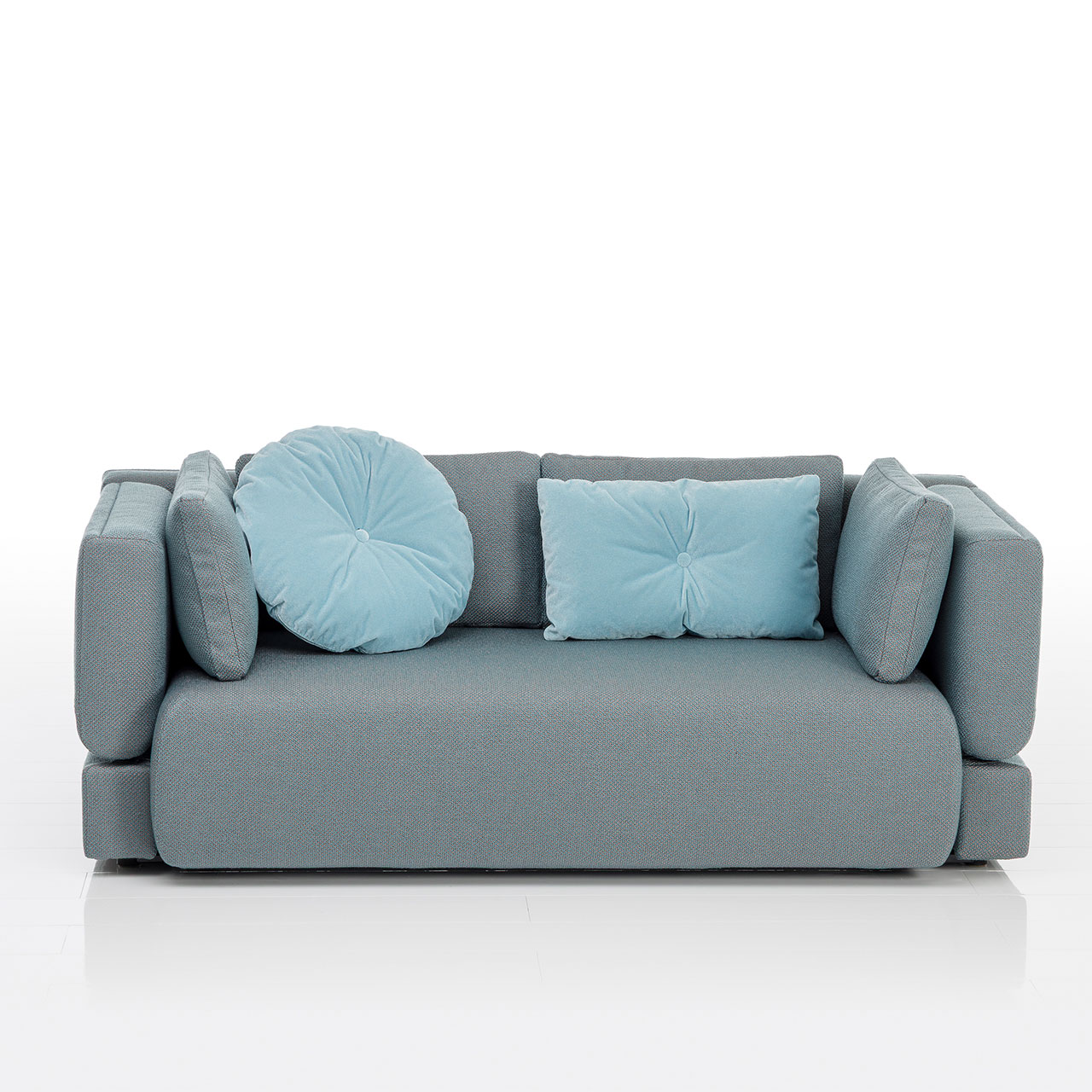 Bodennahes grau-grünes Sofa mit drei eckigen und einem runden Kissen. Die Armlehnen sind abklappbar.