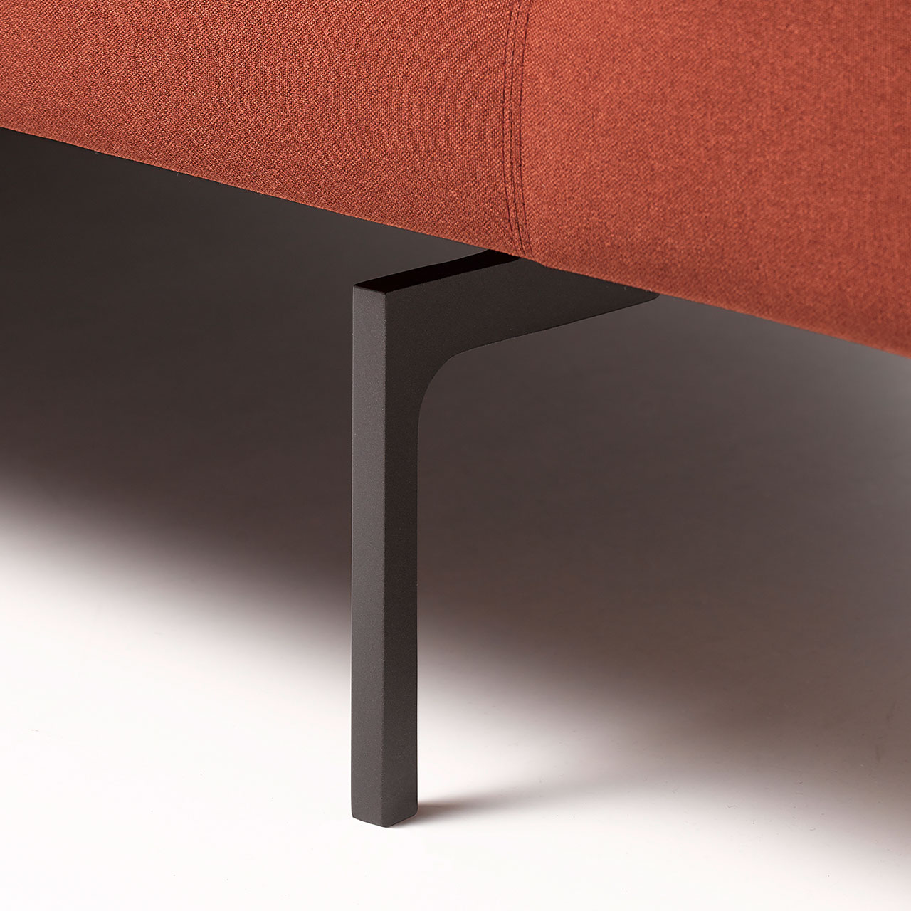 Detailaufnahme eines schwarz lackierten Einzelfußes an einem roten Sofa