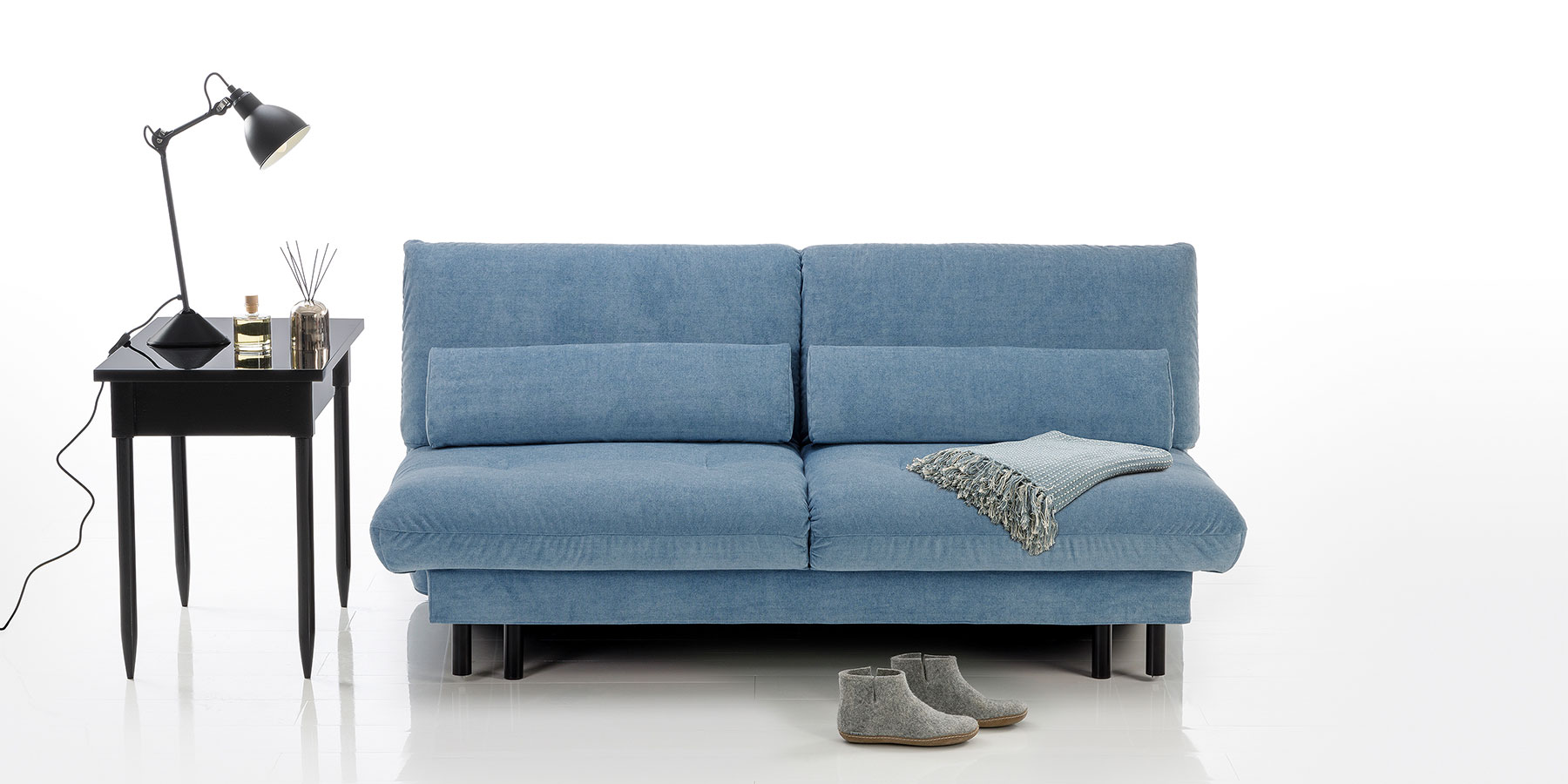 Ein hellblaues Bettsofa mit schwarzen Metallfüßen. Das Sofa ist in der Mitte durch eine Teilungsnaht gegliedert. 