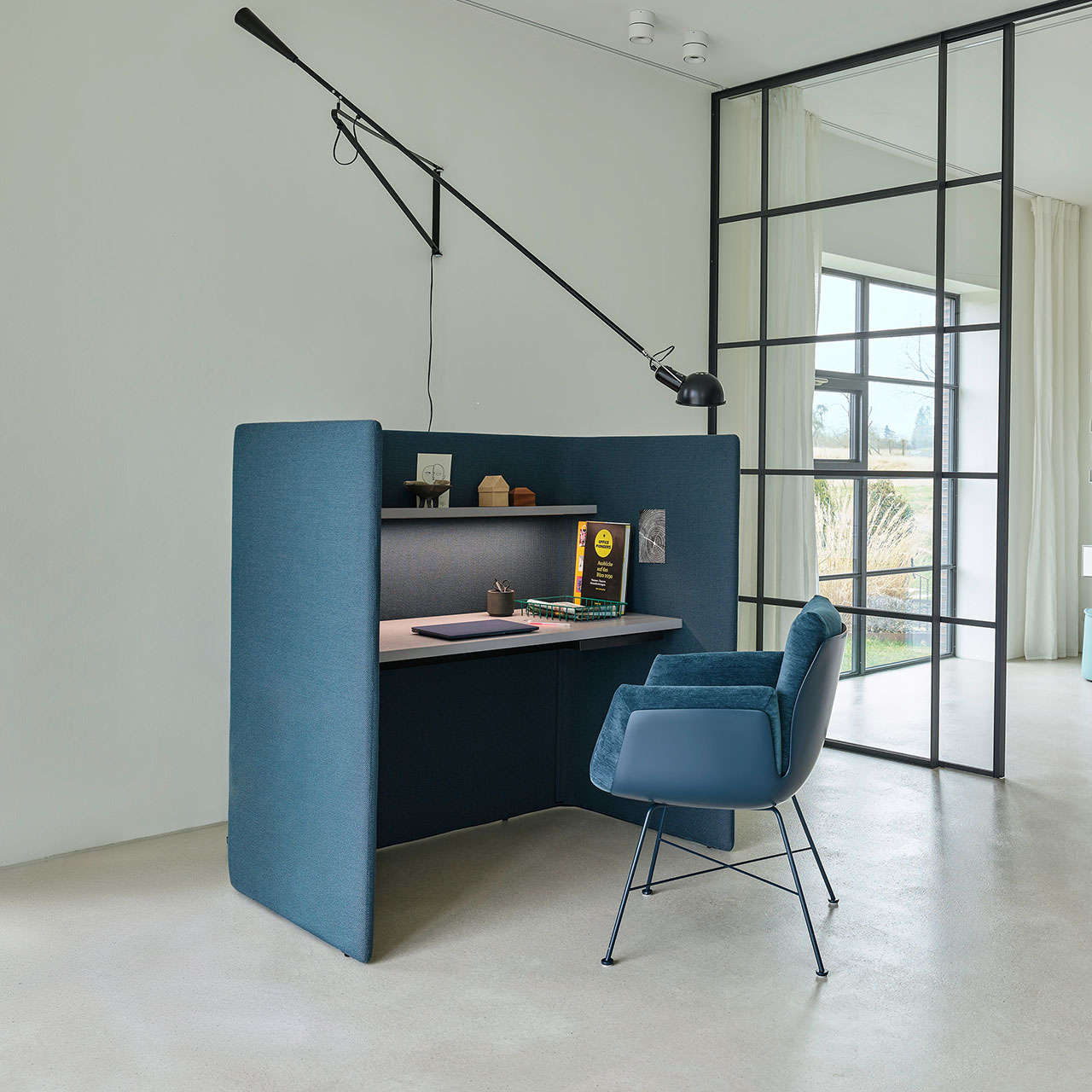 Schreibtisch mit Dekoration und Alvo-Stuhl davor. Die hohe Schreibtischaußenwand und der Stuhl sind aus dem gleichen blauen Stoff gefertigt.