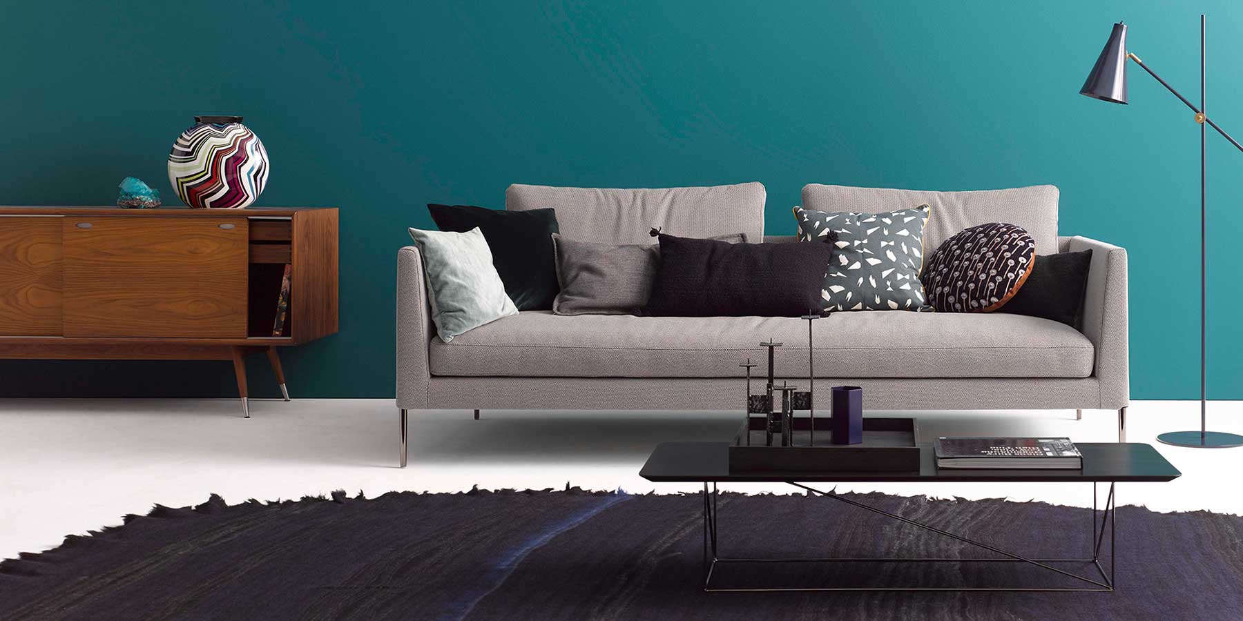 Graues Sofa mit vielen Kissen dekoriert auf hohen Chromfüßen