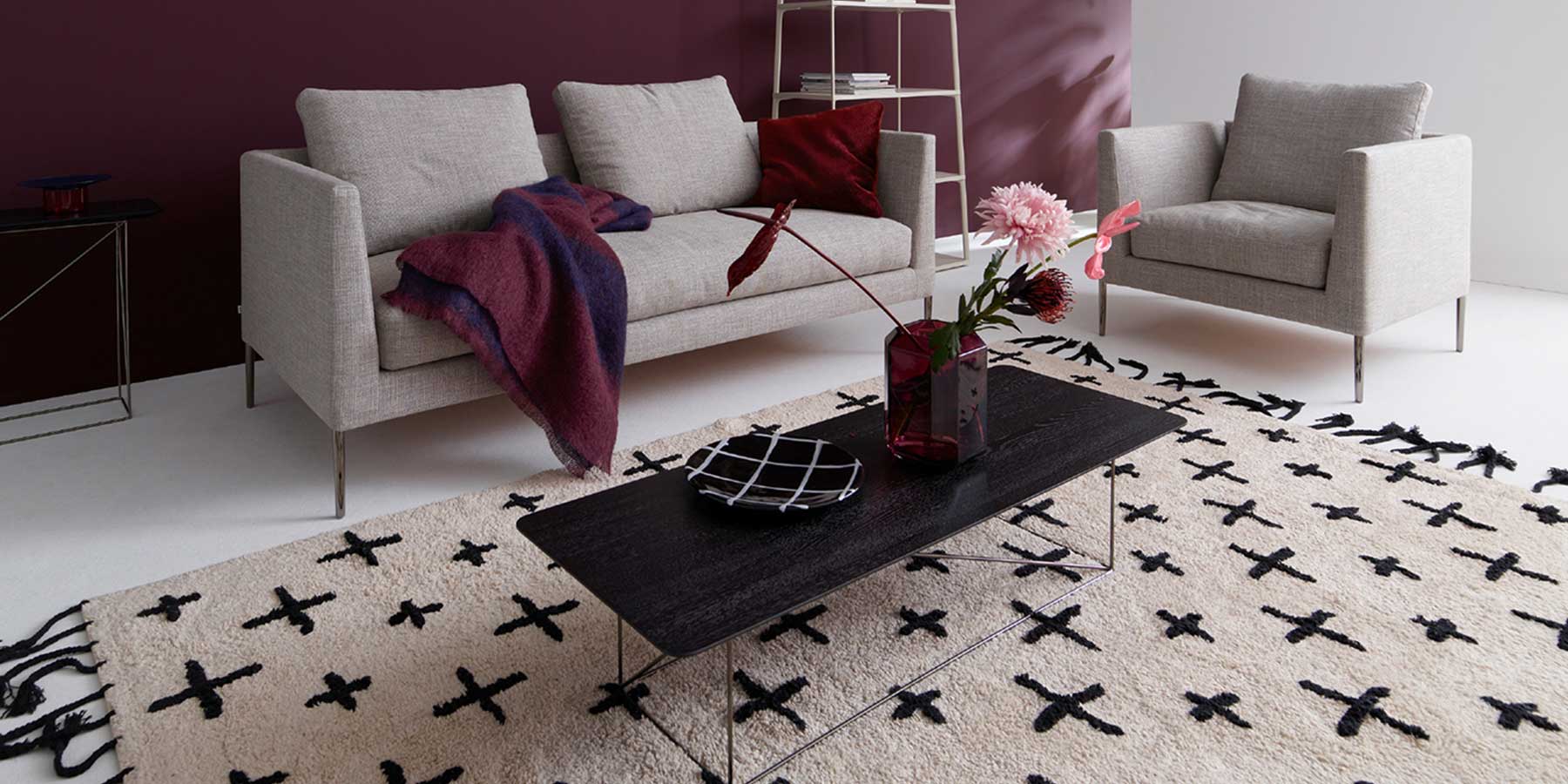 Links ein Zweisitzer-Sofa und rechts ein Sessel aus grauem Stoff mit hohen Füßen