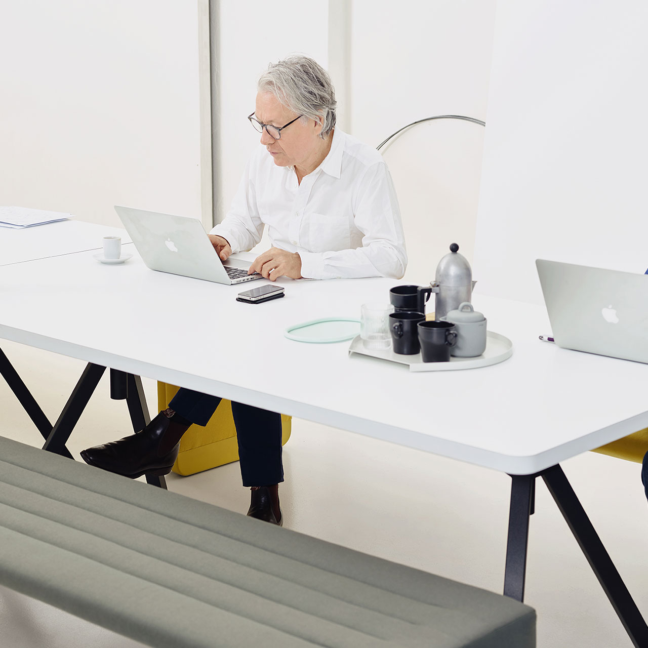 Mann sitzt an Level Tisch mit weißer Platte und schwarzem Zargengestell und arbeitet am Laptop