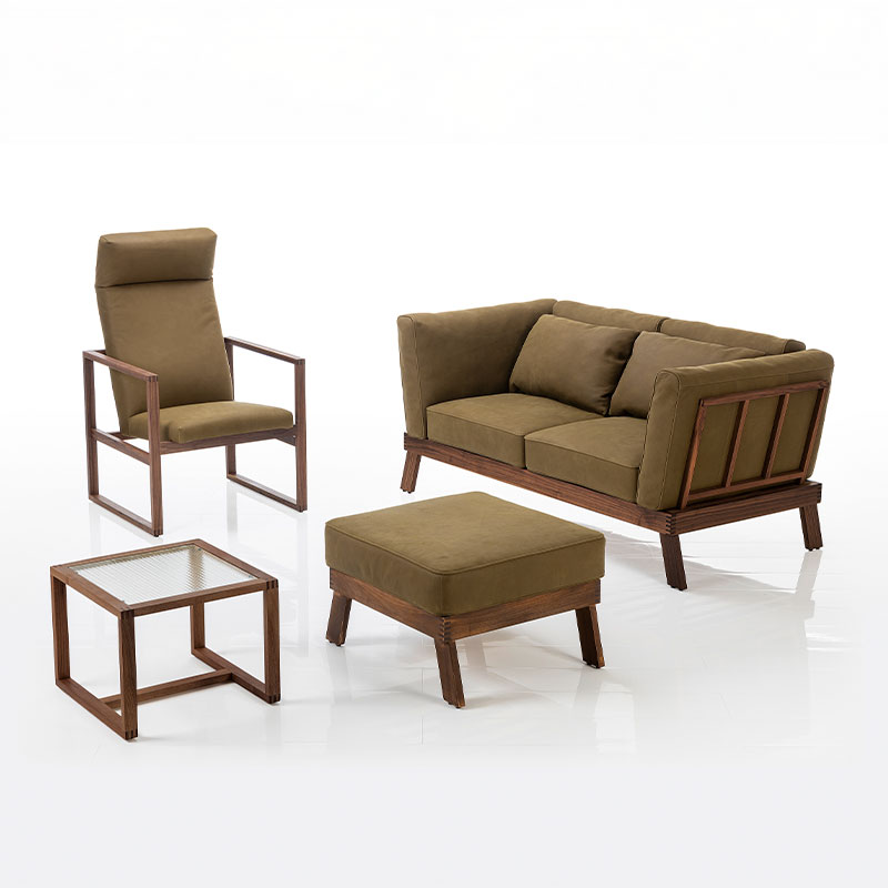 Ein Sessel, ein Sofa, ein Hocker und ein Beistelltisch stehen beisammen. Die Rahmen sind aus dunklem Holz, die Polstermöbel sind mit olivgrünem Stoff bezogen.