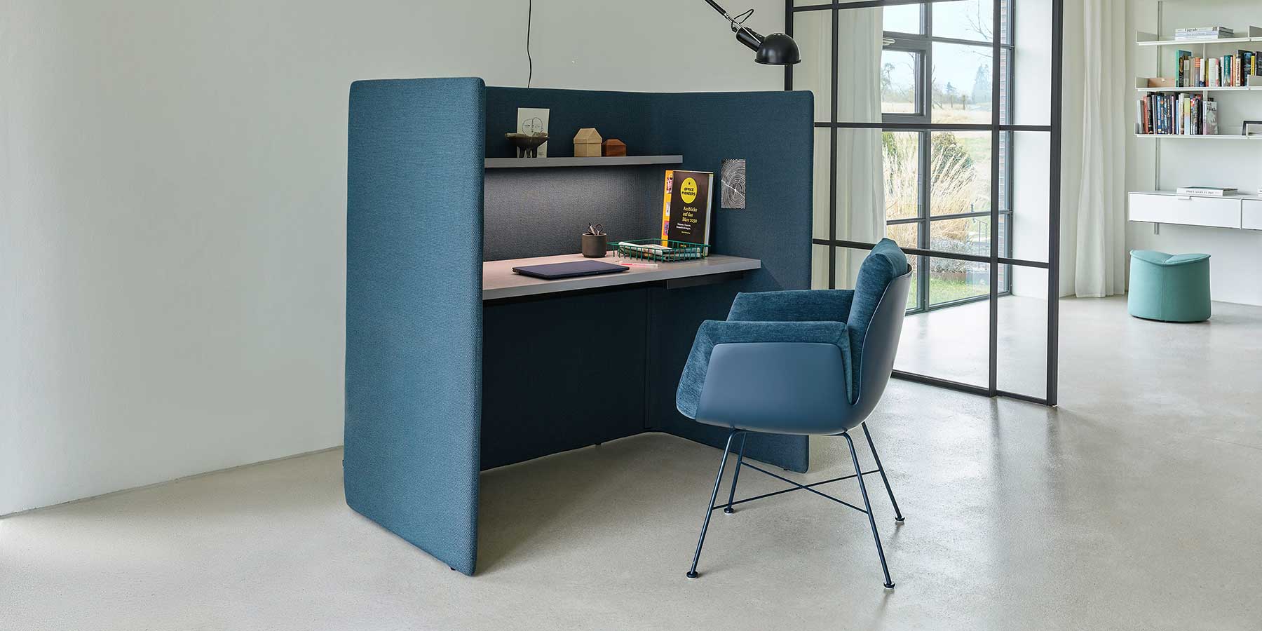 Schreibtisch mit blau gepolsterter Außenschale, davor ein im passenden Stoff bezogener Alvo-Stuhl