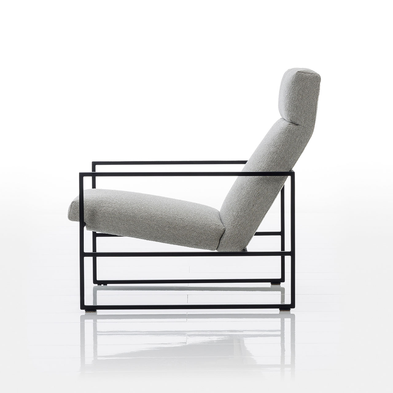 Seitliche Sicht auf einen tiefen Lounge-Sessel mit schwarz pulverbeschichtetem Metallrahmen. Die Sitz- und Rückenpolster des Stuhls sind mit beigem Stoff bespannt. 
