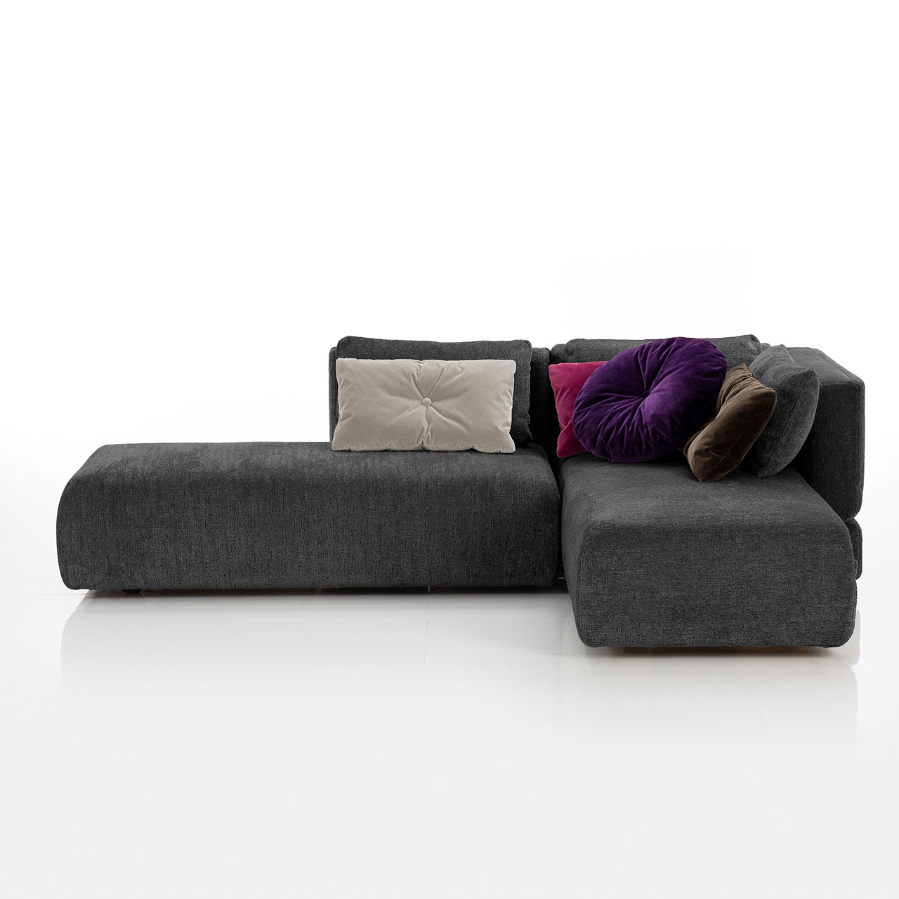 Bodennahes schwarzes Eckofa mit Drehsofa links und Longchair rechts. Auf dem Sofa liegen drei eckige und eine rundes Kissen.