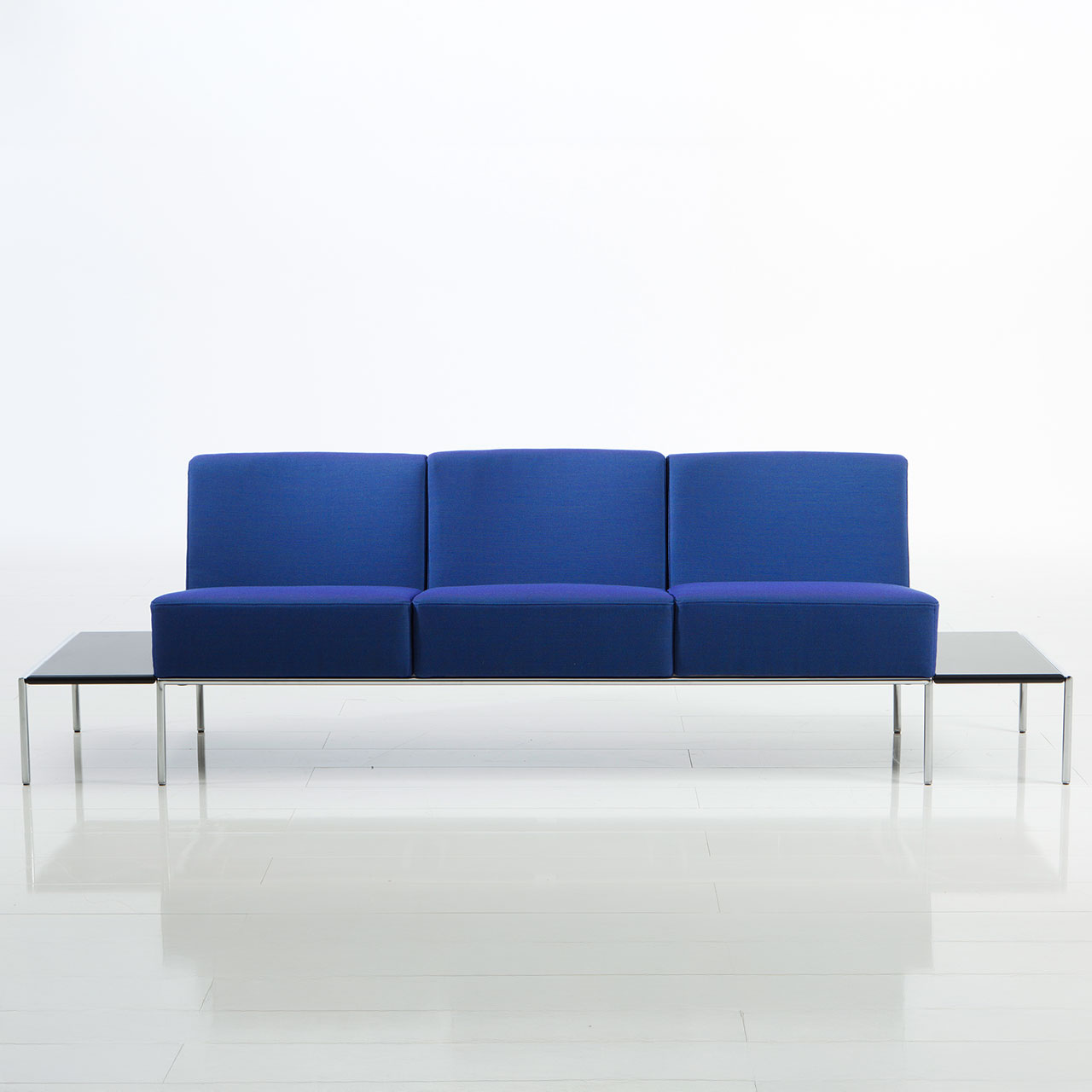 Mit blauem Stoff bezogene Bank von brühl add1 mit jeweils einer Ablage auf der rechten und linken Seite.
