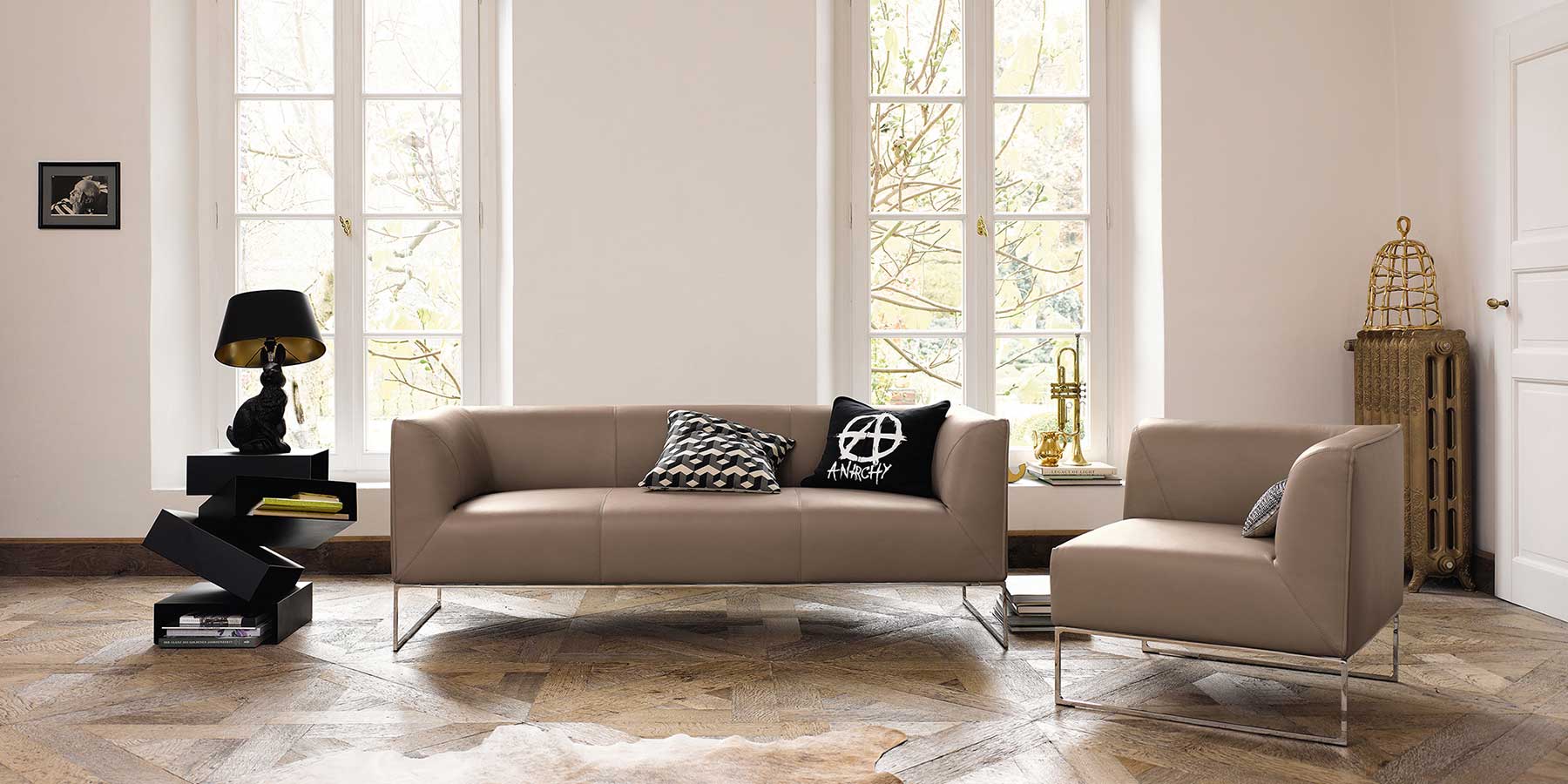 Beiges Ledersofa auf Kufen mit passenem Sessel mit Lehne auf einer Seite in einem Wohnzimmer mit Parkettboden