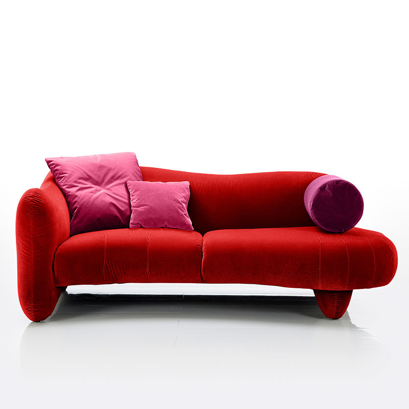 Rotes, sanft geschwungenes Sofa mit einer bis zum Boden durchgehenden Armlehne links und einer Rolle als Armlehne rechts.