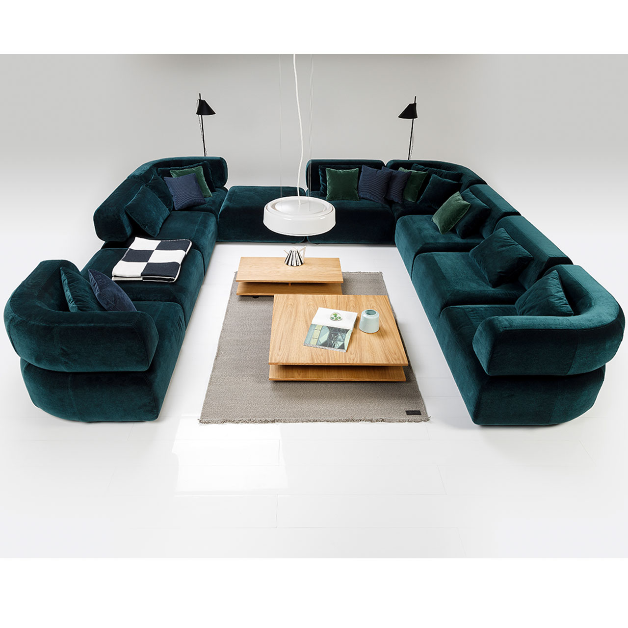 U-förmige Sitzgarnitur in tiefgrünem Stoff mit zwei passenden Tischen in warmem Holz in der Mitte.