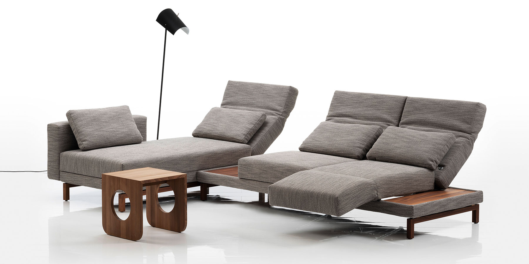 Eine Eckgarnitur bestehend aus einem Longchair und einem Anstellsofa. Der Stoff ist milchkaffebraun, das Gestell ist aus dunklem Holz.