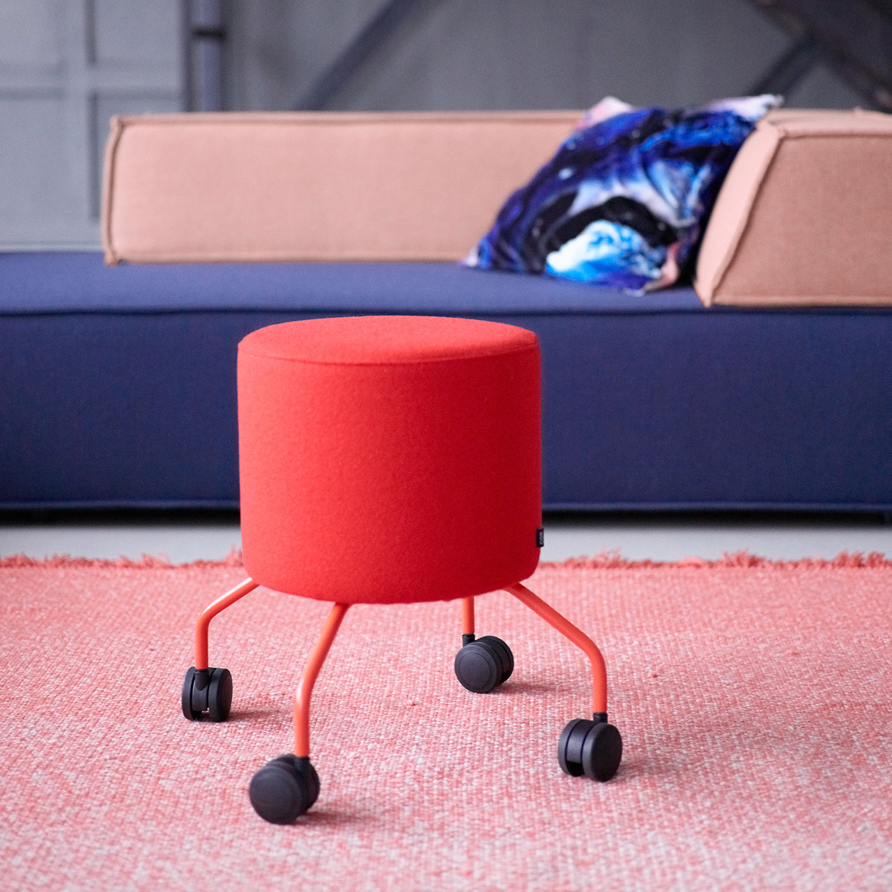 Roter zylinderförmiger Hocker auf roten Beinen mit Rollen vor COR Trio Sofa