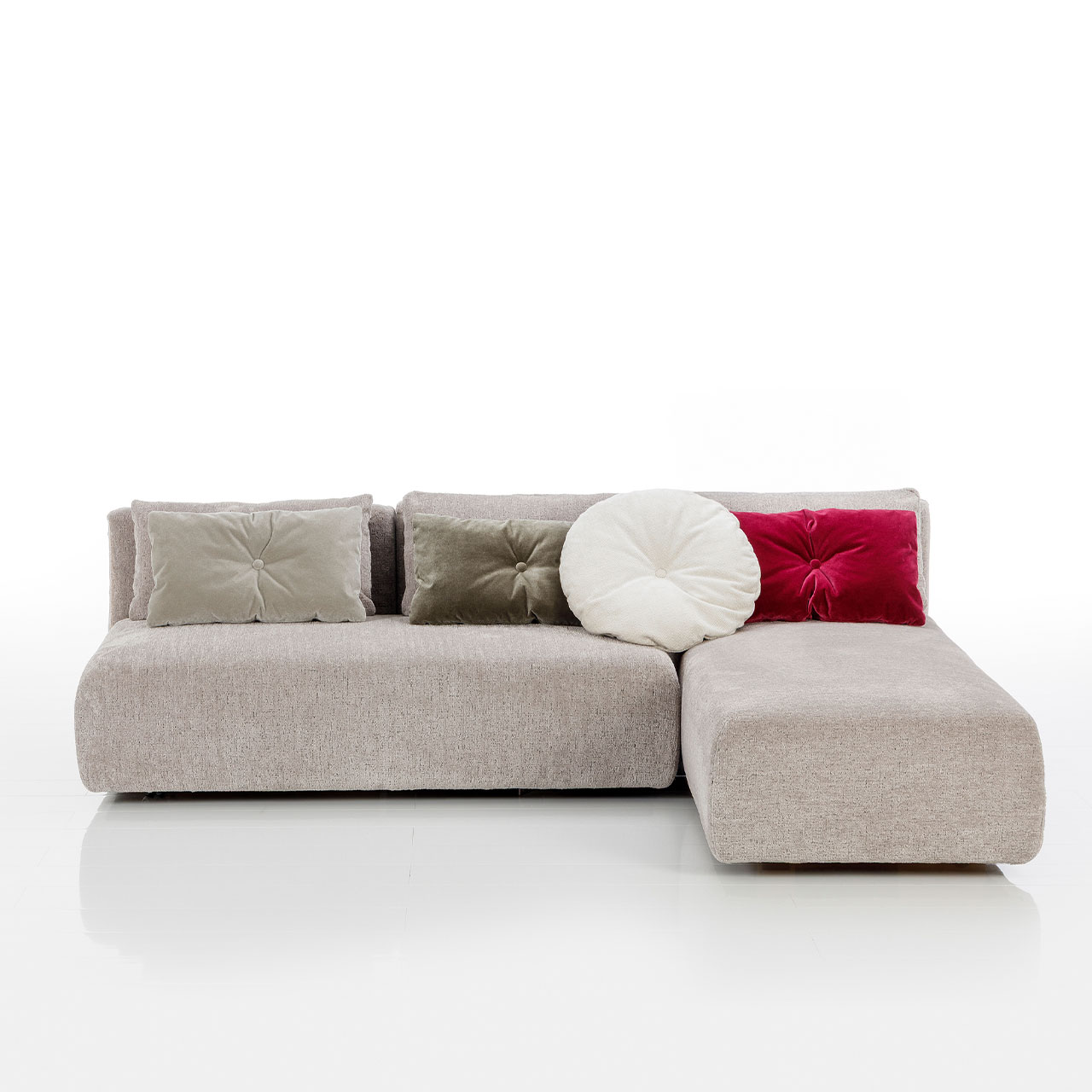 Bodennahes beiges Eckofa mit Drehsofa links und Longchair rechts. Auf dem Sofa liegen drei eckige und eine rundes Kissen.