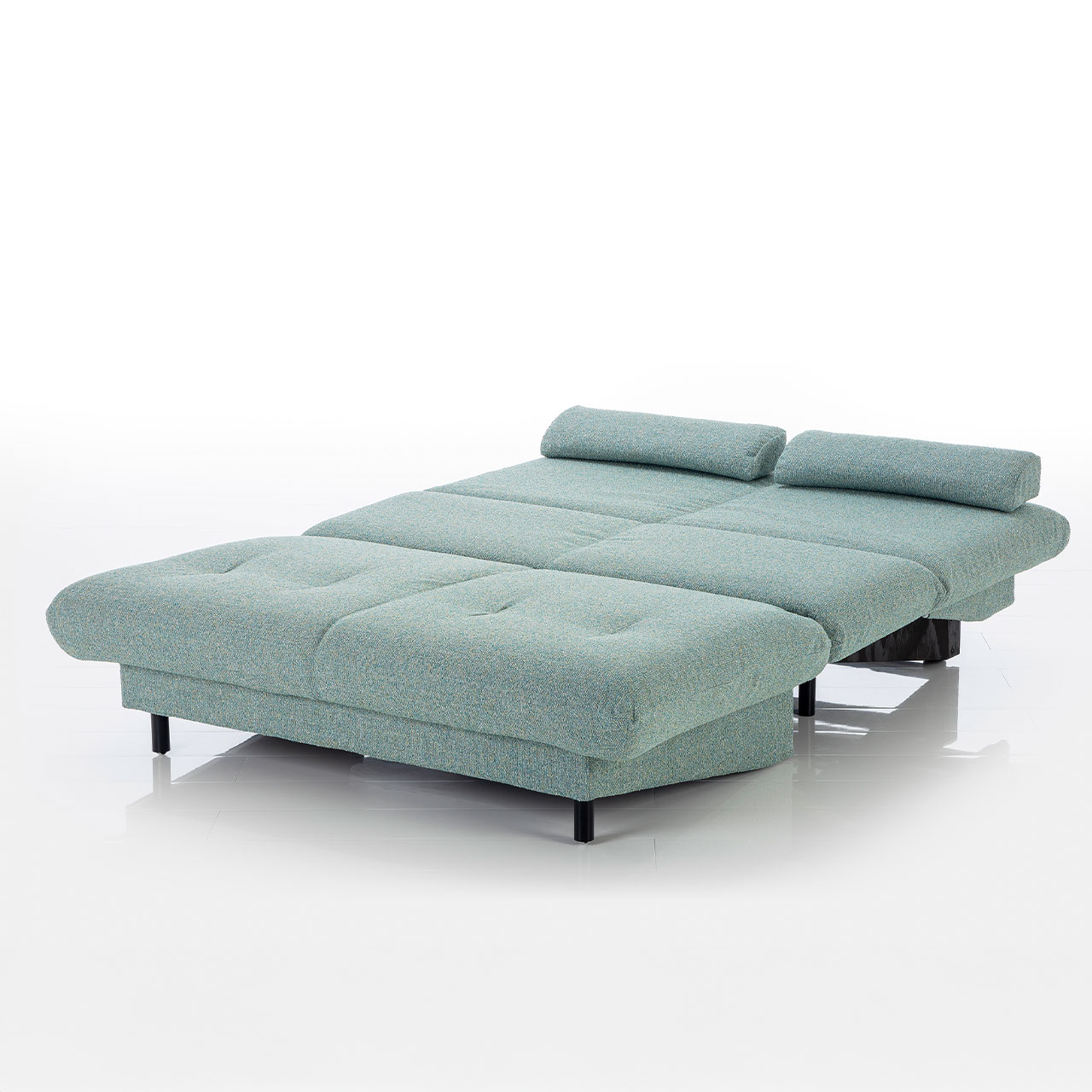 Zur Liegefläche ausgezogenes Bettsofa ohne Armlehnen. Der Stoff ist salbeigrün.