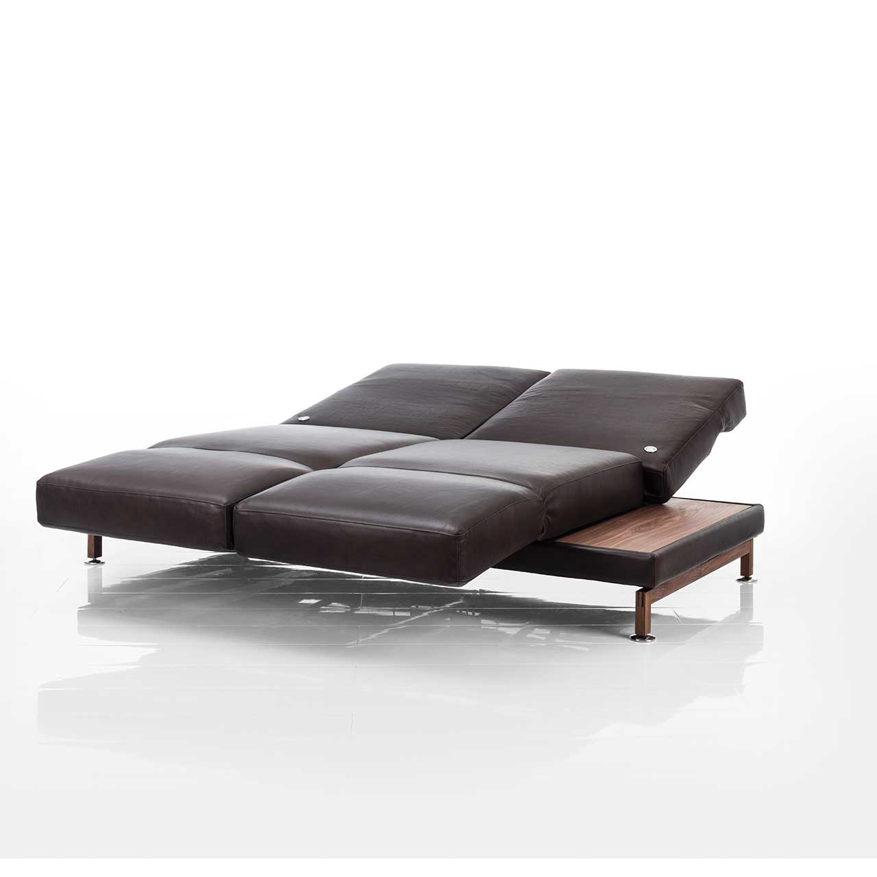 Dunkelbraunes Ledersofa. Die Armlehnen sind vorgeschwenkt, die Rückenlehnen komplett abgesenkt, so dass eine Liegefläche entsteht. Rechts und links sind Ablageflächen aus dunklem Holz integriert.