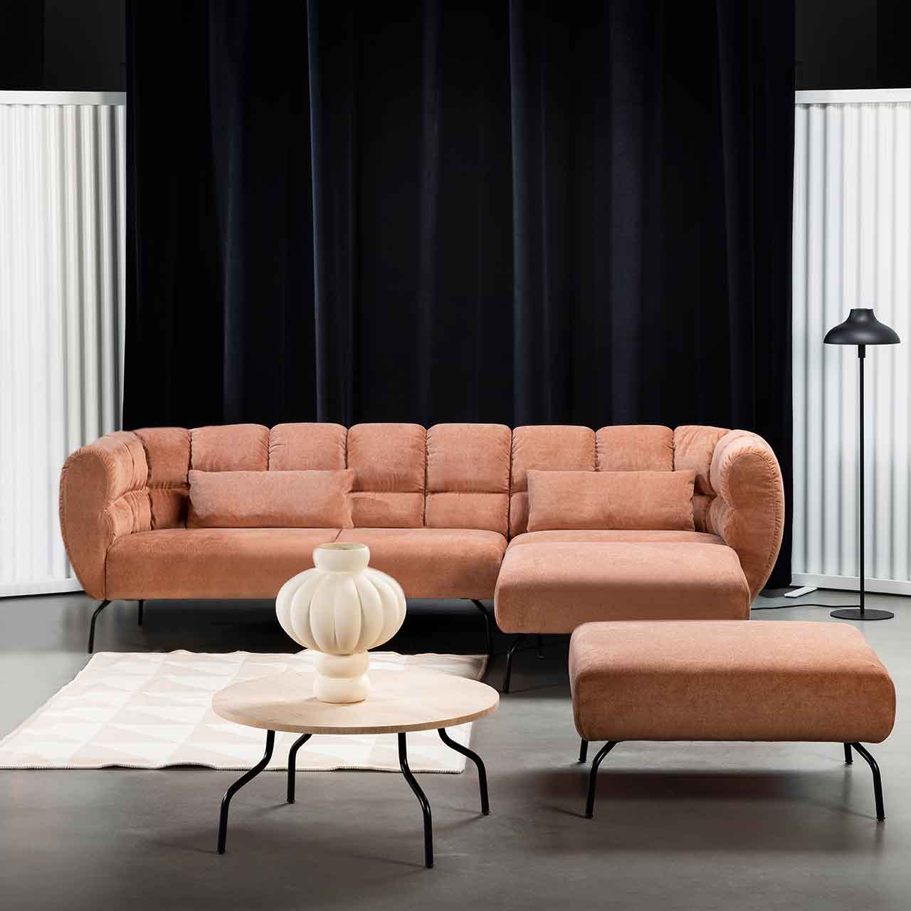 Eckgarnitur von brühl magnolia mit Longchair rechts in rotbraunem Leder mit schwarzen Füßen. Rechts vor der Garnitur steht ein quadratischer Hocker. Zentral vor der Garnitur steht ein runder Beistelltisch mit heller Holzplatte.