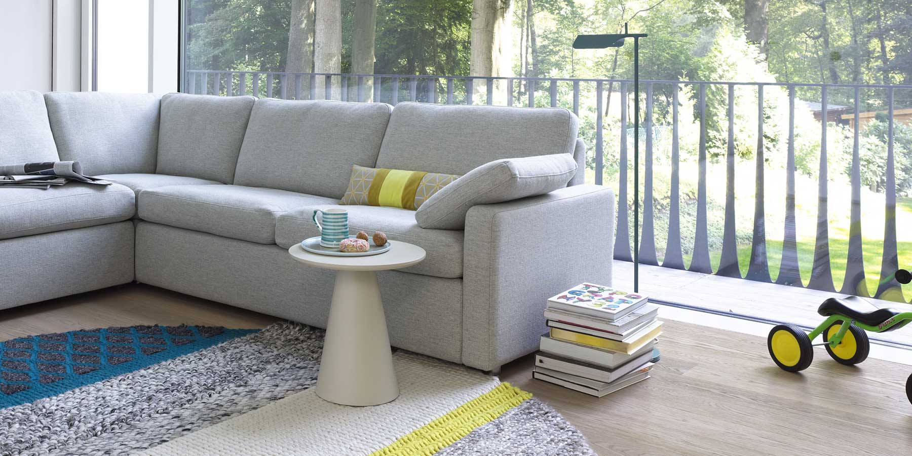 Beistelltisch mit konischem Fuß und runder Platte vor einem grauen Sofa.