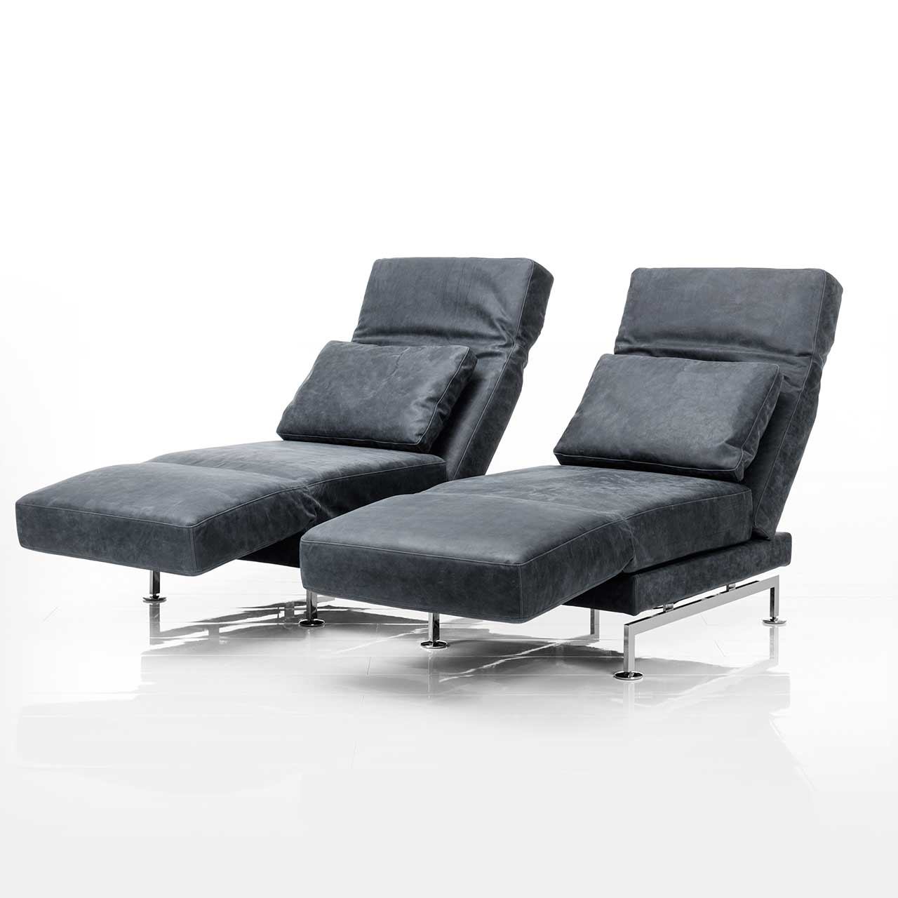 Zwei Relaxsessel der Serie brühl moule in grauem Leder sind mit einem Einhängetisch zu einer Garnitur verbunden. Beide Rückenlehnen sind halb abgesenkt und die Armlehnen zur Relaxposition vorgeschwenkt.
