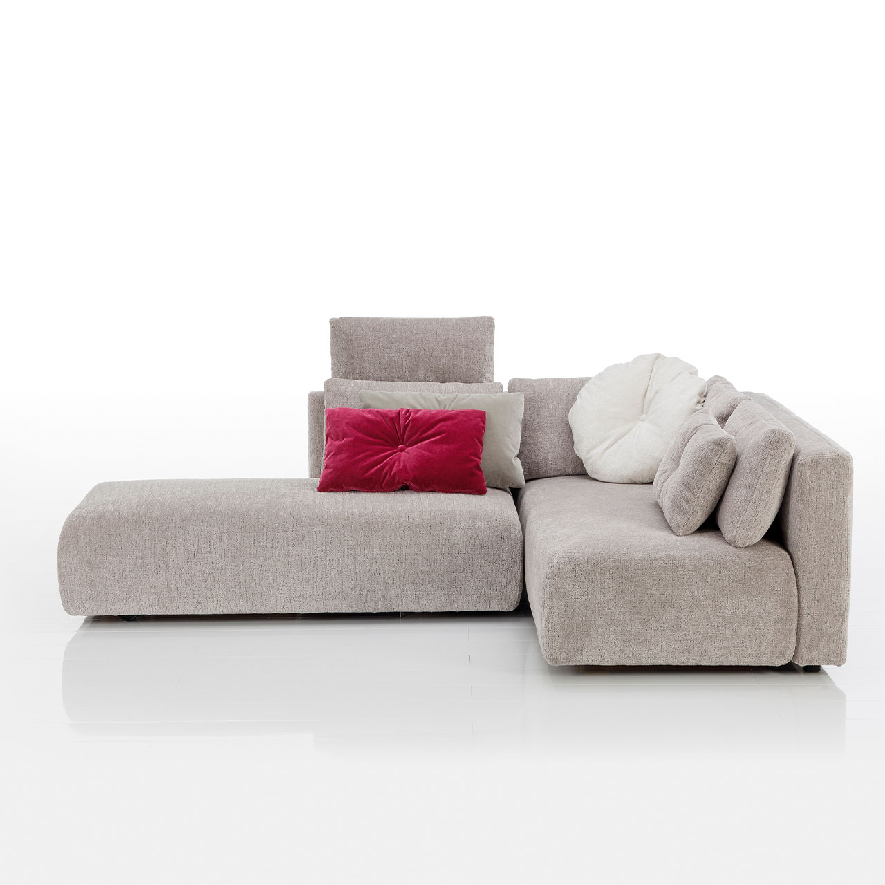 Bodennahes beiges Eckofa mit Drehsofa links und Longchair rechts. Auf dem Sofa liegen drei eckige und eine rundes Kissen.