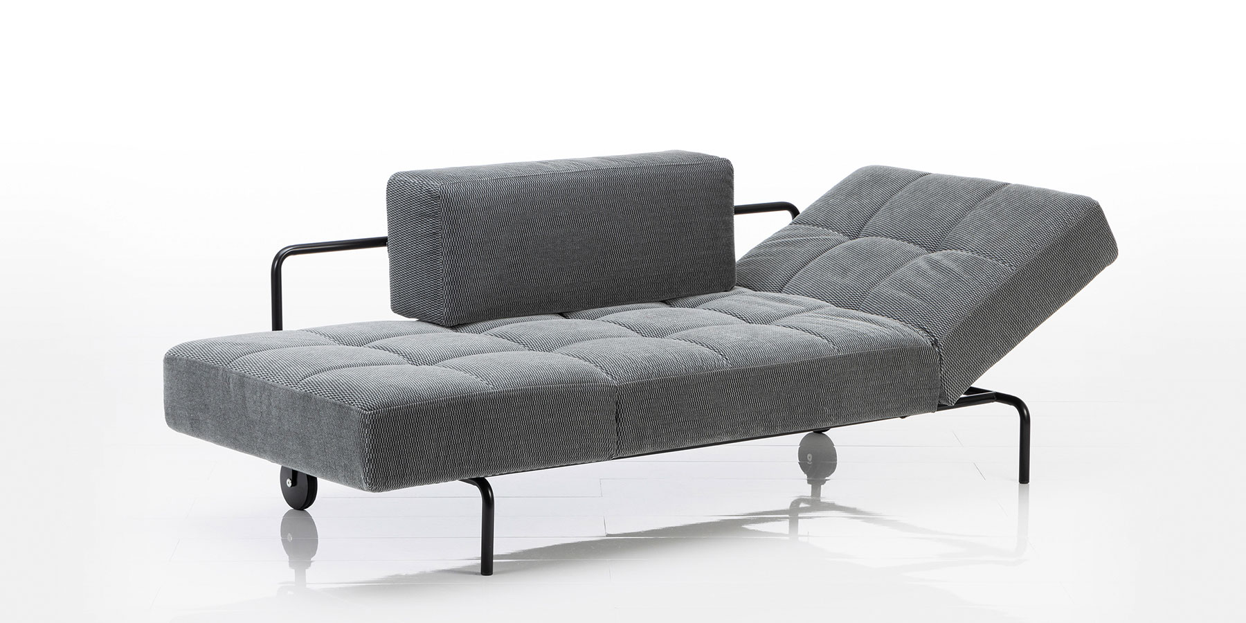 Eine Recamiere mit schwarzem Untergestell. Das Polster ist gesteppt, das Rückenlehnkissen ist kubisch und hinten nur angelegt.