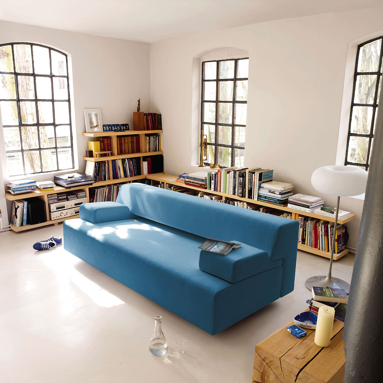 Sofa aus hellblauem Stoff mit zwei Armlehnkissen rechts und links in einem Wohnzimmer.