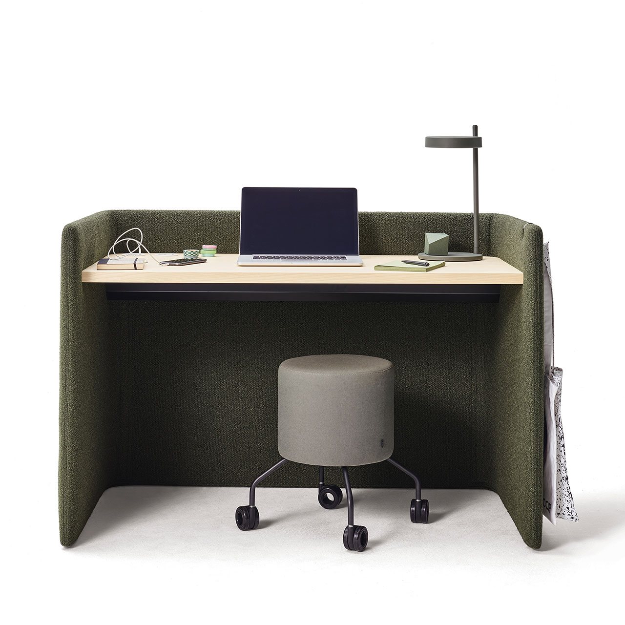 Schreibtisch mit niedriger Polster-Umrandung aus Stoff mit heller Holz-Tischplatte. Dekoration mit Notebook und Büroutensilien. Davor ein grauer Drop-Hocker.
