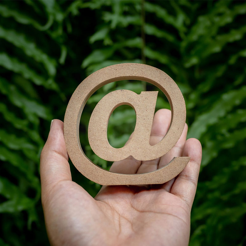 Eine Hand hält ein hölzernes @ Zeichen.