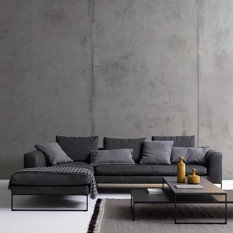 Graues Ecksofa mit Recamiere links auf schwarzen Metallkufen. Sofa ist mit Kissen dekoriert.