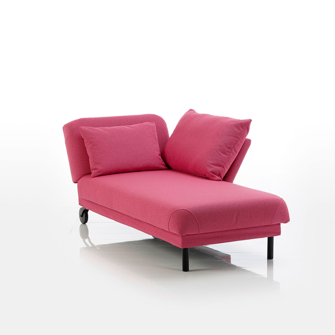 Recamiere in pinkem Stoff mit Rollen an der Kopfseite und zylindrischen Füßen an der Fußseite. Das Kopfteil ist höhenverstellbar. Rechts vom Kopfteil ist eine abklappbare Armlehne angebracht.