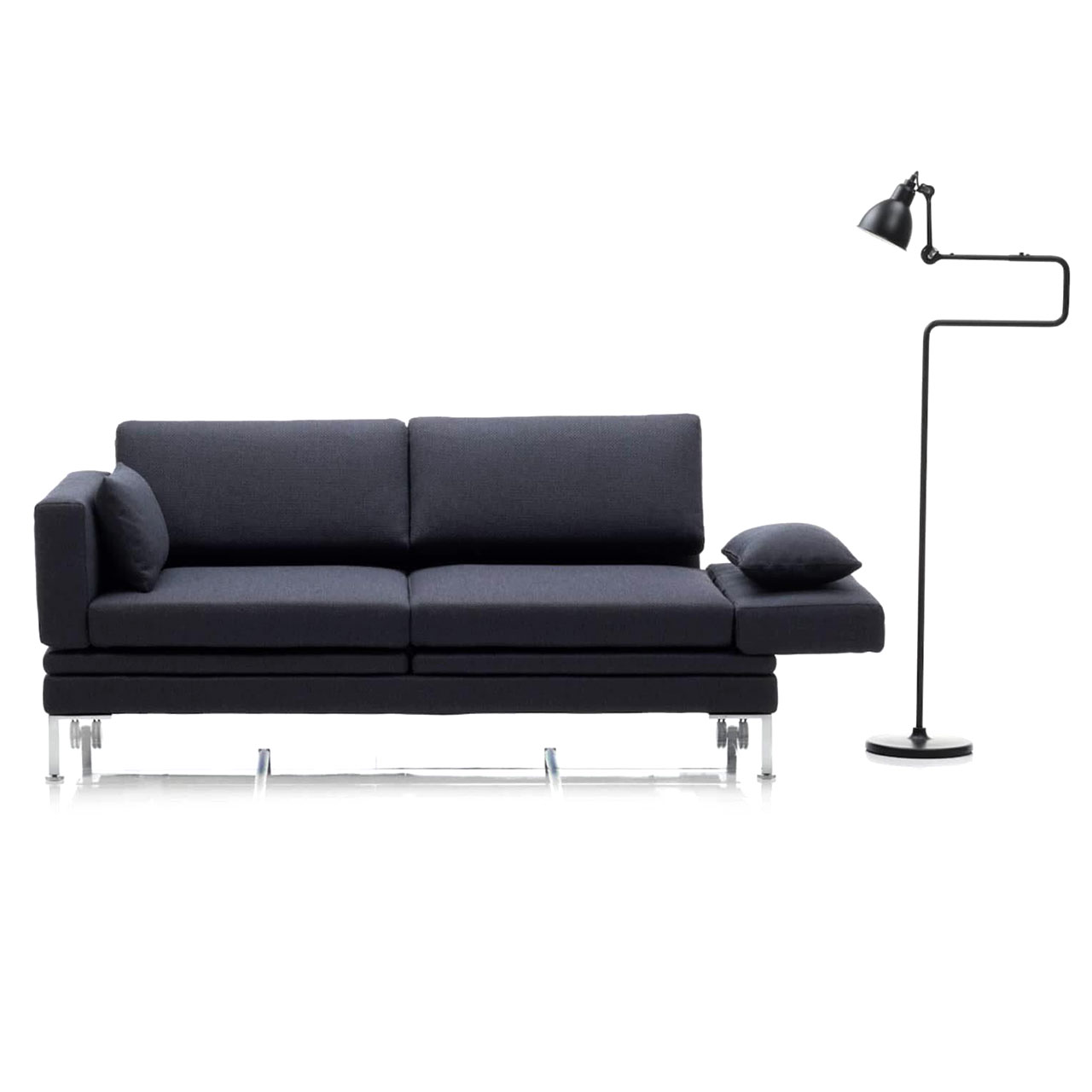 Ein dunkelblaues Sofa mit waagrecht abgeklappter rechter Armlehne. Auf der rechten Seite des Sofas steht eine Stehlampe.