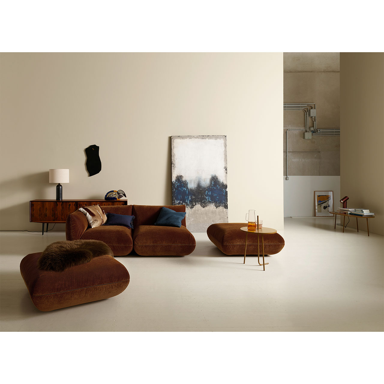 Milieuaufnahme zeigt Sofa aus zwei Teilen und zwei Hocker mit Deko in einem Wohnzimmer