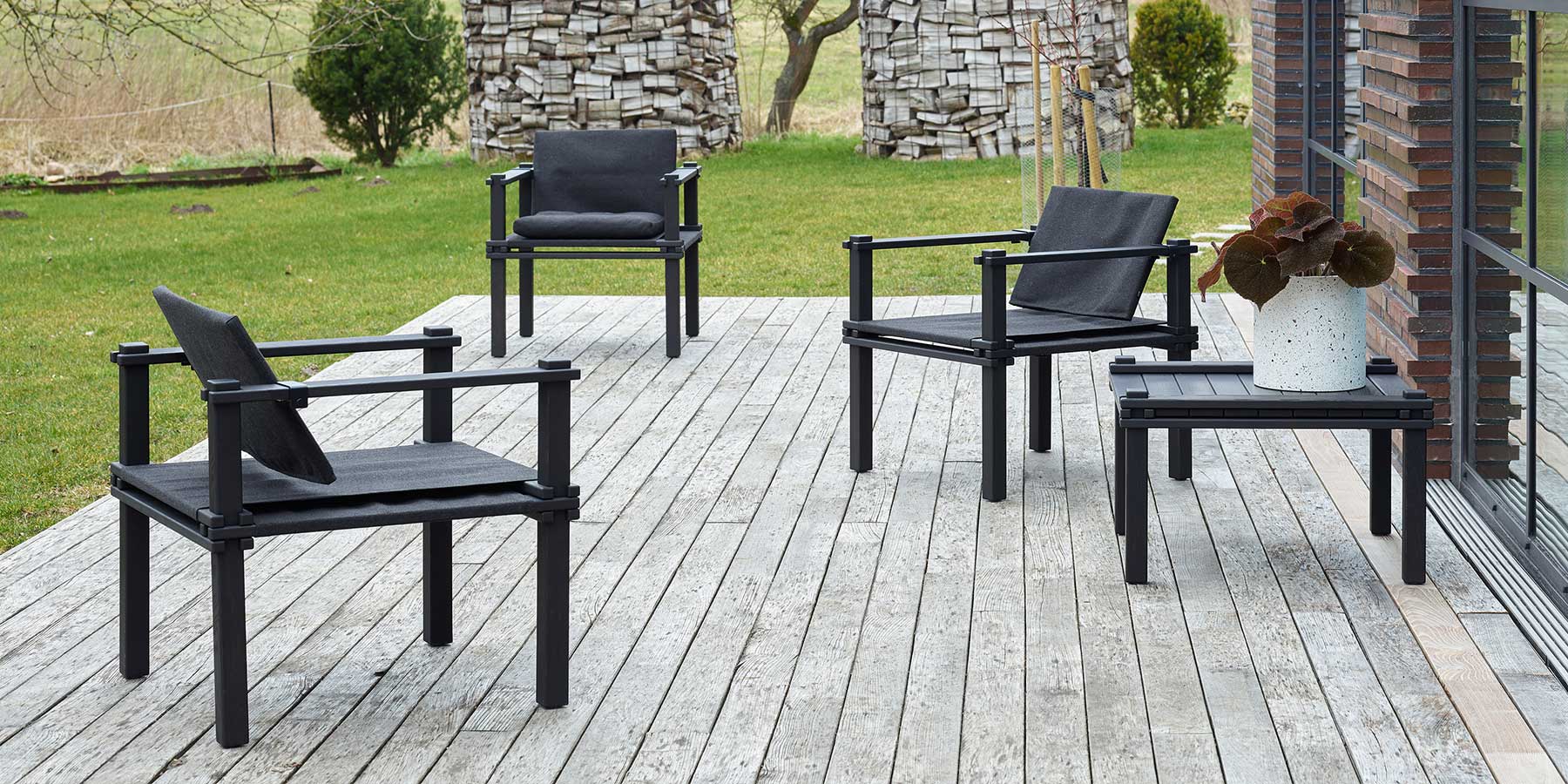 Drei schwarz geölte Stühle mit schwarzem Stoffbezug mit dem passenden Tisch auf einer Terrasse aus Holzdielen