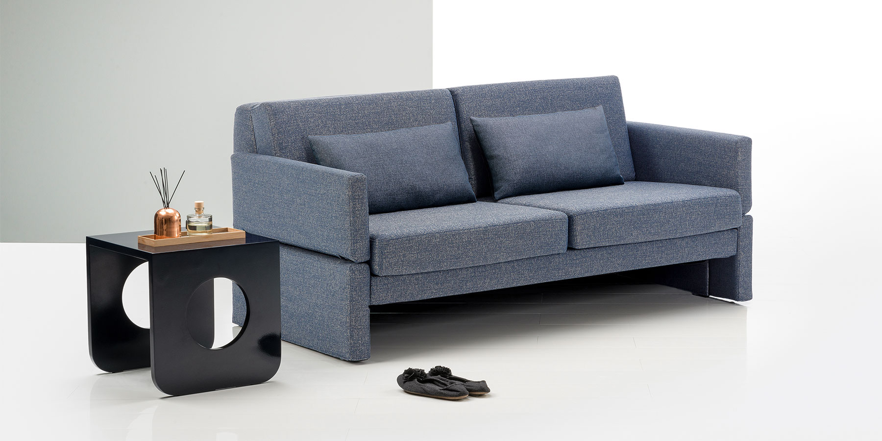 Ein graublaues, eckiges Sofa mit schmalen gepolsterten Armlehnen und zwei langen Rückenkissen.