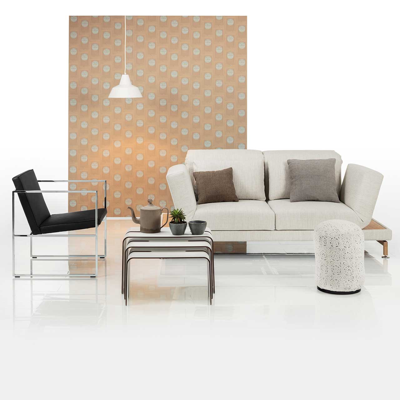 Ambientebild. Sofa der Serie brühl moule in weißem Stoff, rechts davor ein runder Hocker. Vorne links steht ein Sessel der Serie grace mit schwarzem Lederbezug.