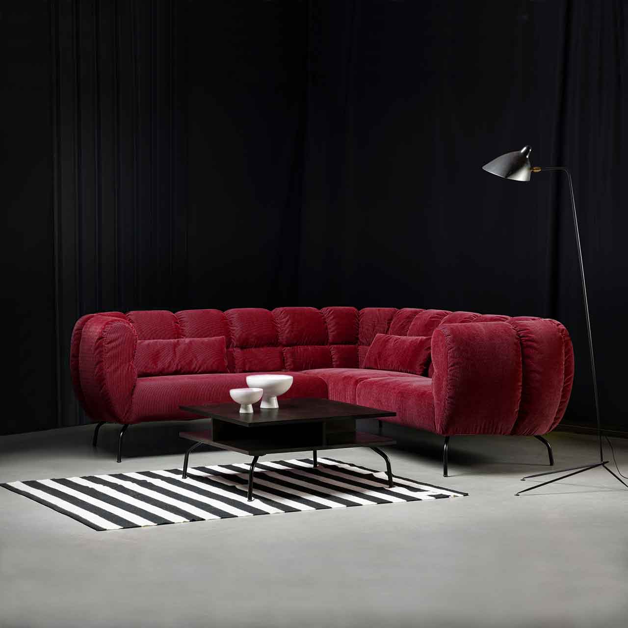 Ambientebild: Eckgarnitur von brühl magnolia in dunkelrotem Stoff mit schwarzen Metallfüßen. Davor steht ein quadratischer Tisch mit dunkler Tischplatte und schwarzen Metallfüßen.