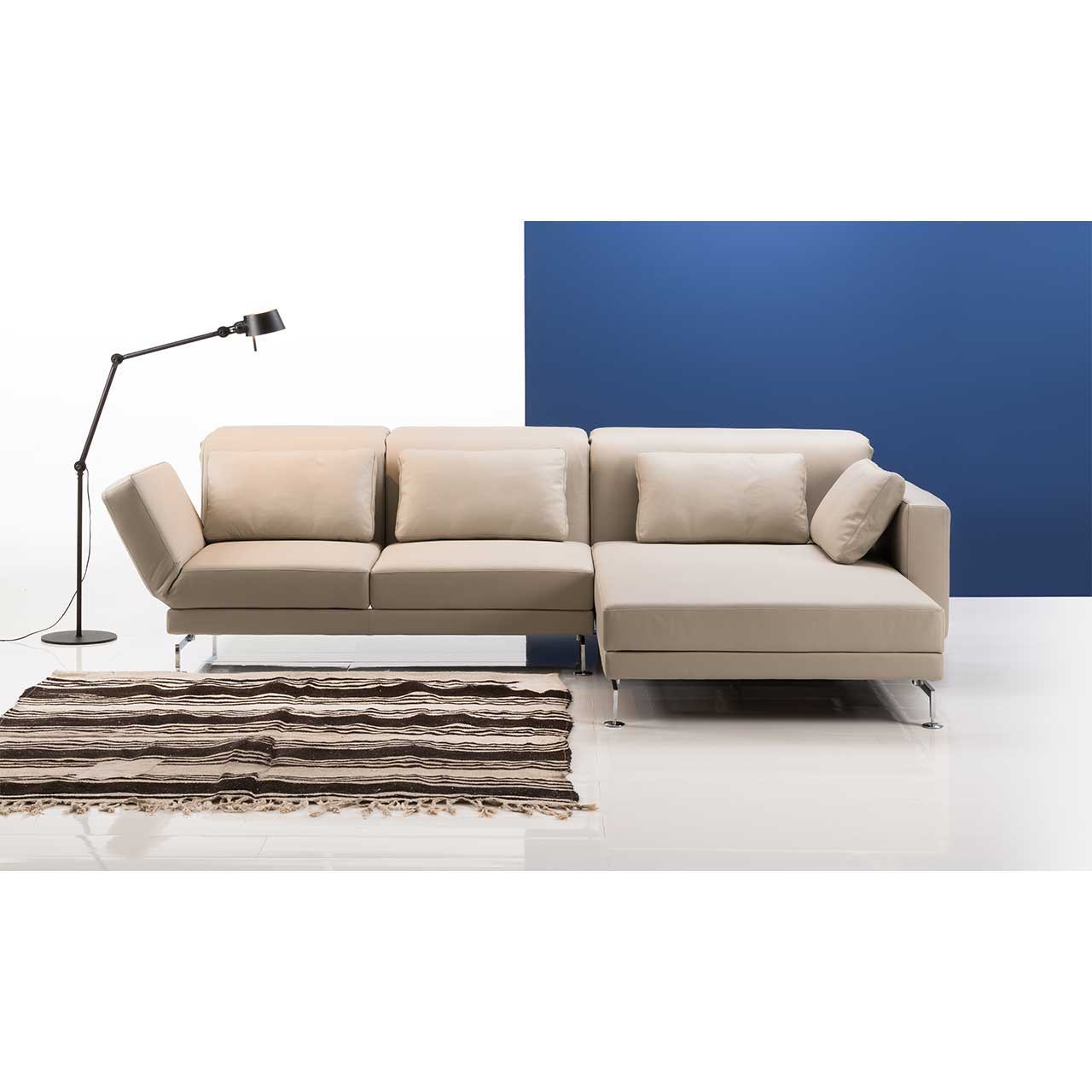 Eckgarnitur mit breitem Longchair rechts in beigem Leder. Links daneben steht eine Lampe, vor der Garnitur liegt ein gestreifter Teppich.
